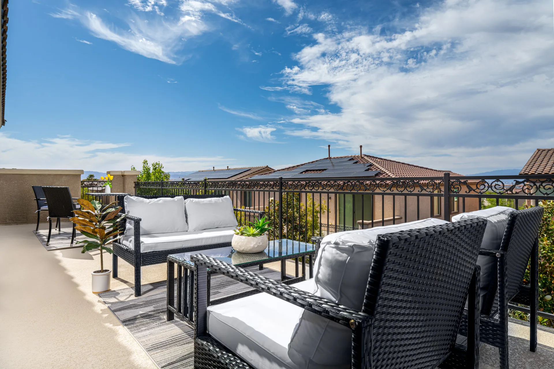 An expansive second-story balcony with wicker seating, white cushions, and a succulent centerpiece, overlooking suburban rooftops.