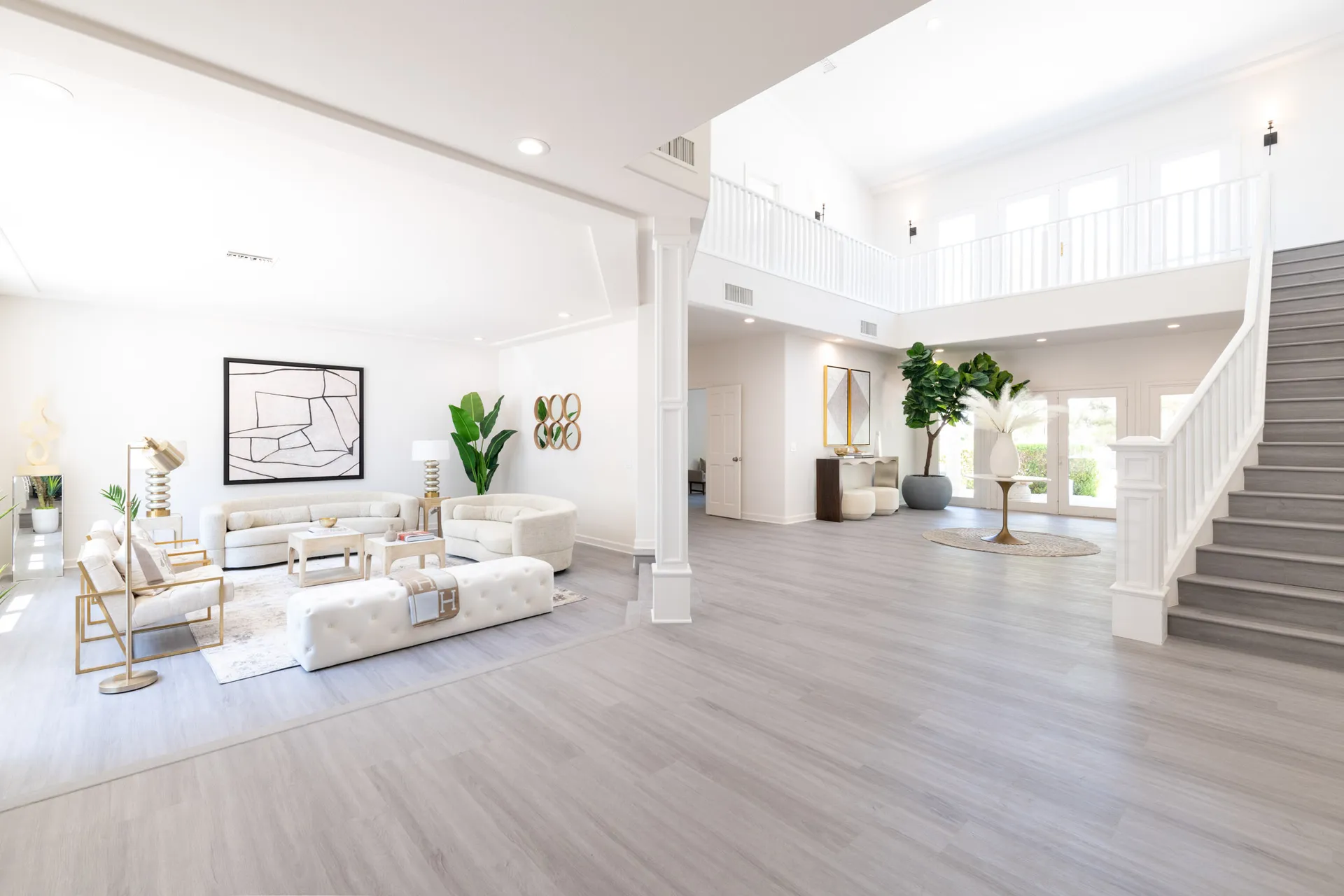 A bright open foyer and living space with neutral seating, gold accent chairs, and a large white staircase.