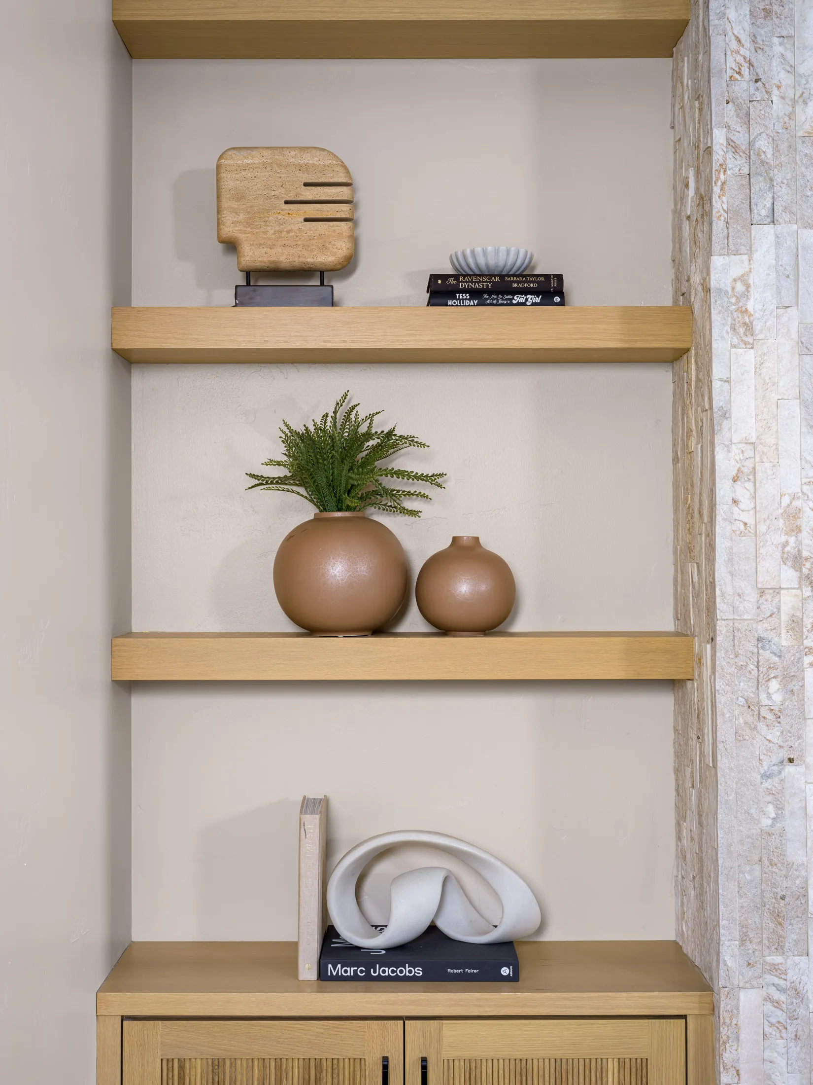 Wooden shelves decorated with a stone sculpture, ceramic vases, books, and a small plant. A textured stone wall is visible alongside the display.