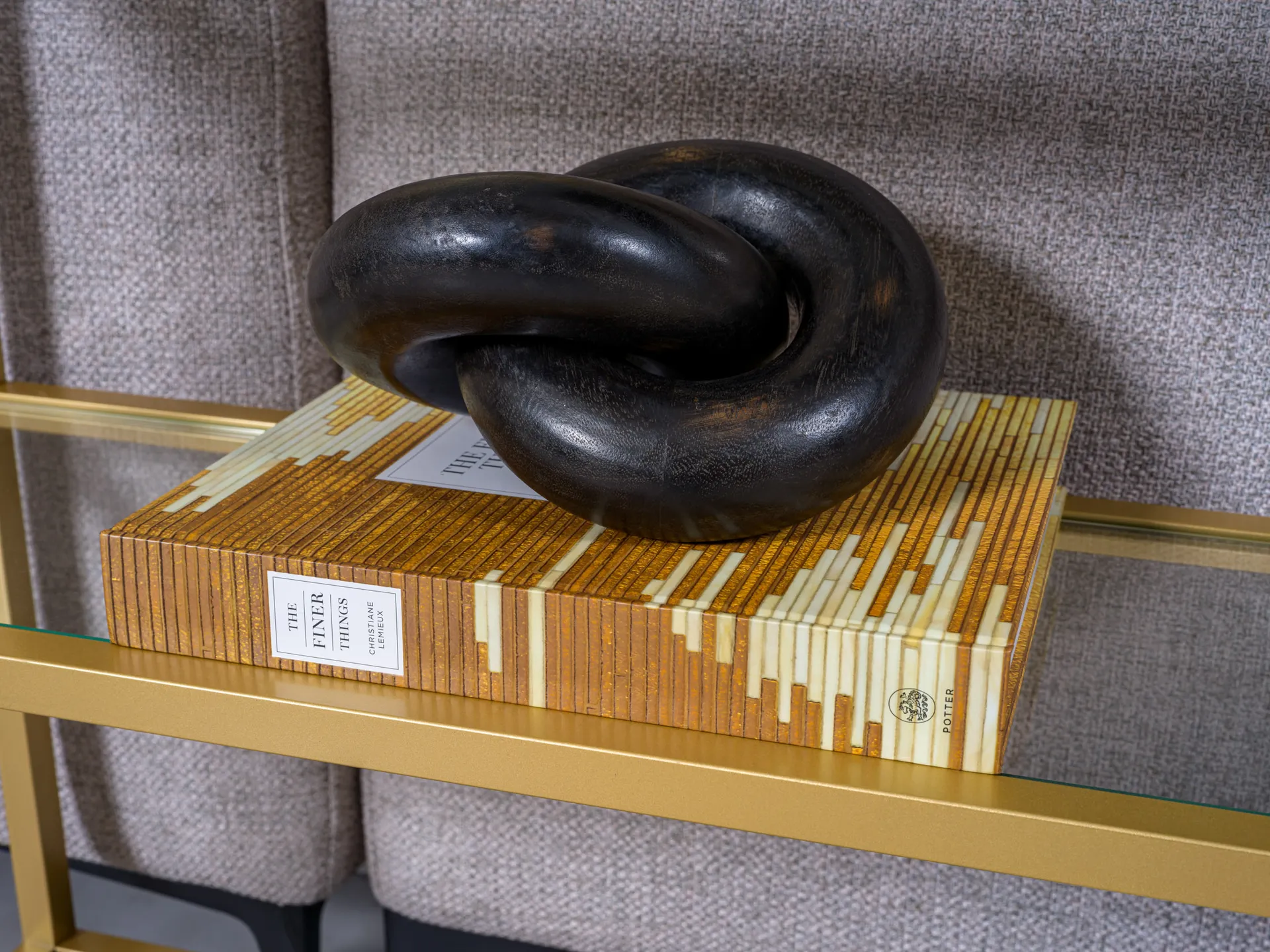 A gold-framed shelf with a rectangular coffee table book topped by a black knot sculpture.
