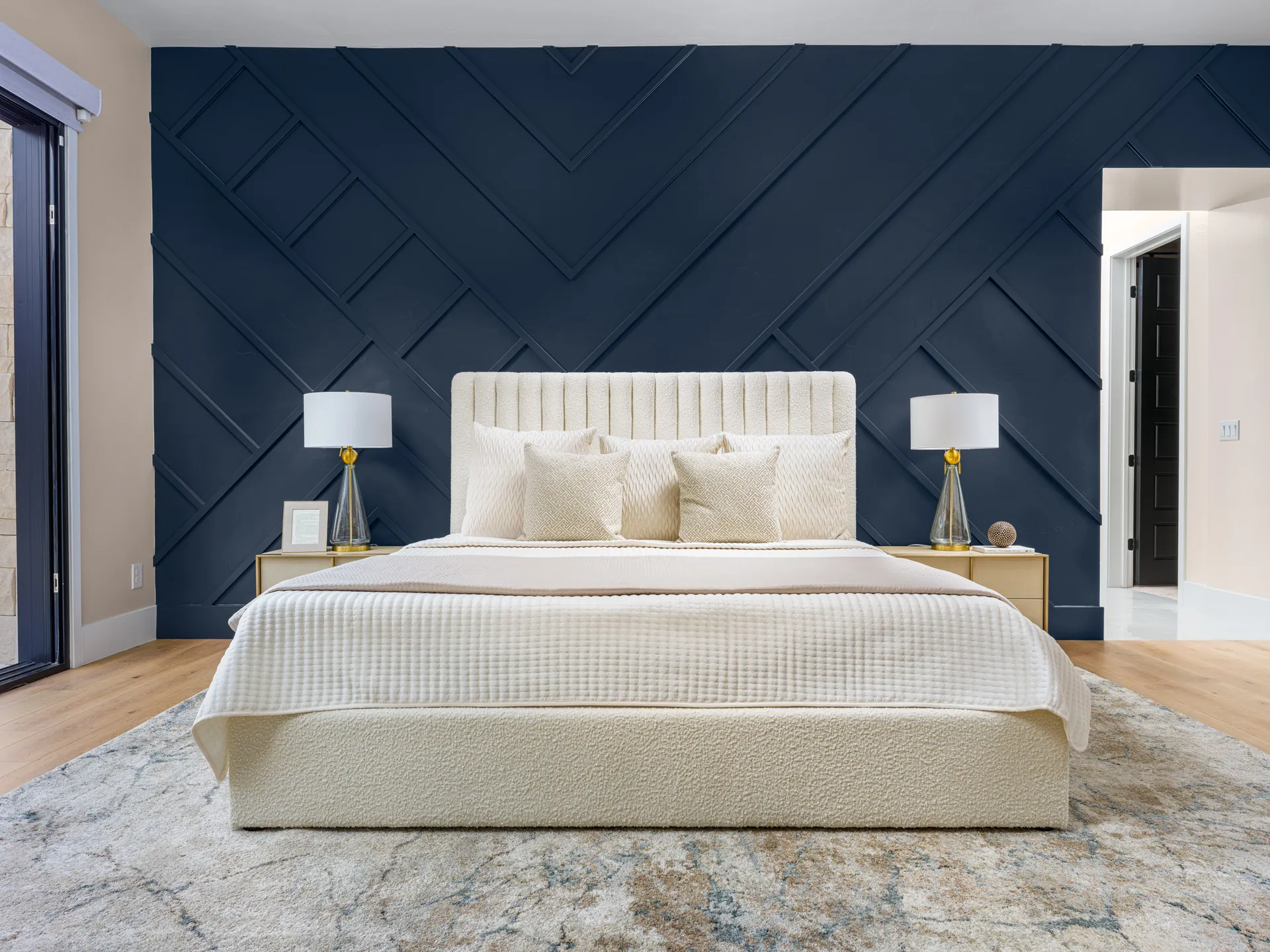A cream upholstered bed with neutral linens against a dark, geometric accent wall, styled by Stately in Las Vegas for a sophisticated focal point.