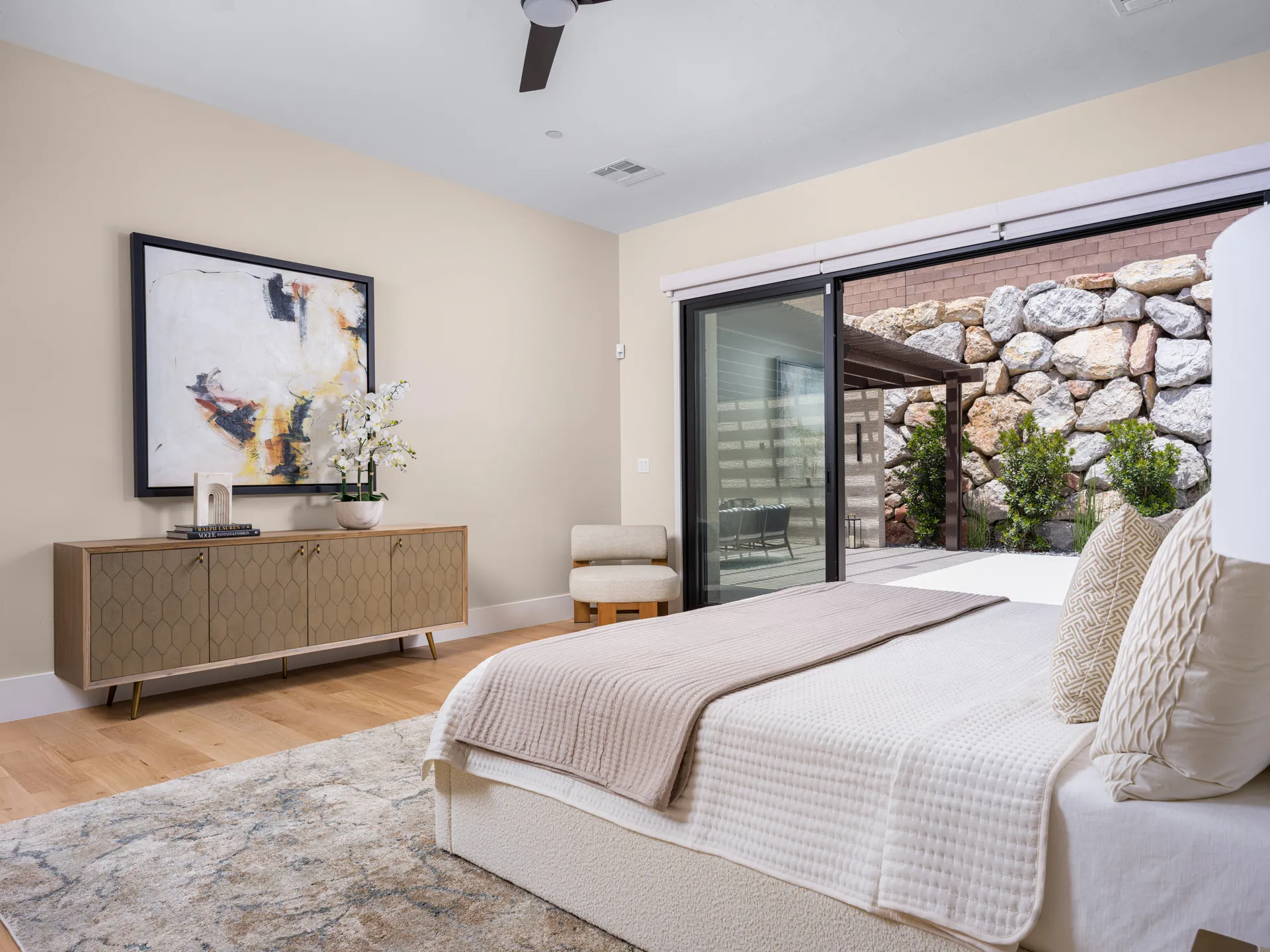 A neutral-toned bedroom with sliding glass doors, featuring a large abstract painting above a modern console. Staged by Stately in Las Vegas for a seamless indoor-outdoor retreat.