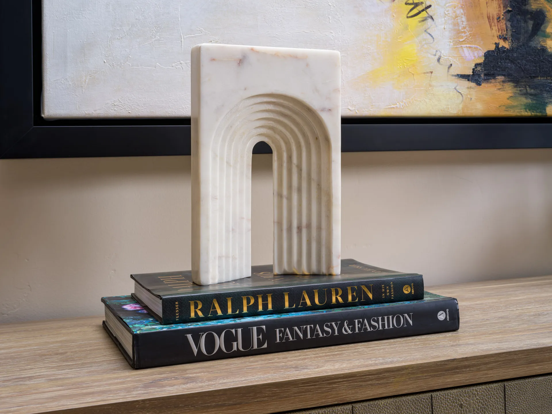 A white marble arch sculpture resting on two coffee table books—Ralph Lauren and Vogue—styled on a wooden console. Staged by Stately in Las Vegas for an elegant, design-forward accent.