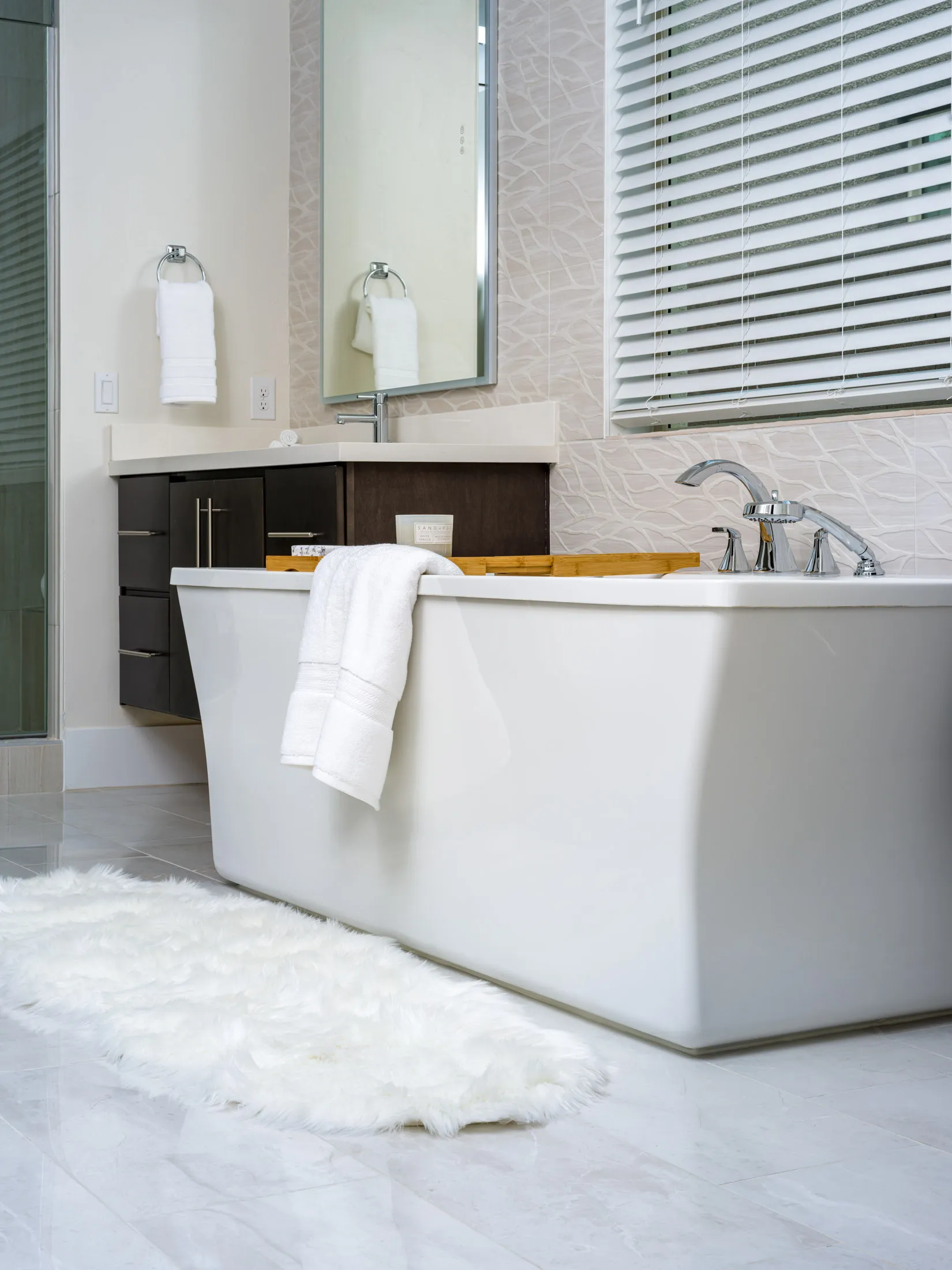 A modern white bathtub with a plush rug and a sleek vanity in a softly lit bathroom. Staged by Stately in Las Vegas to exude spa-like luxury and style.