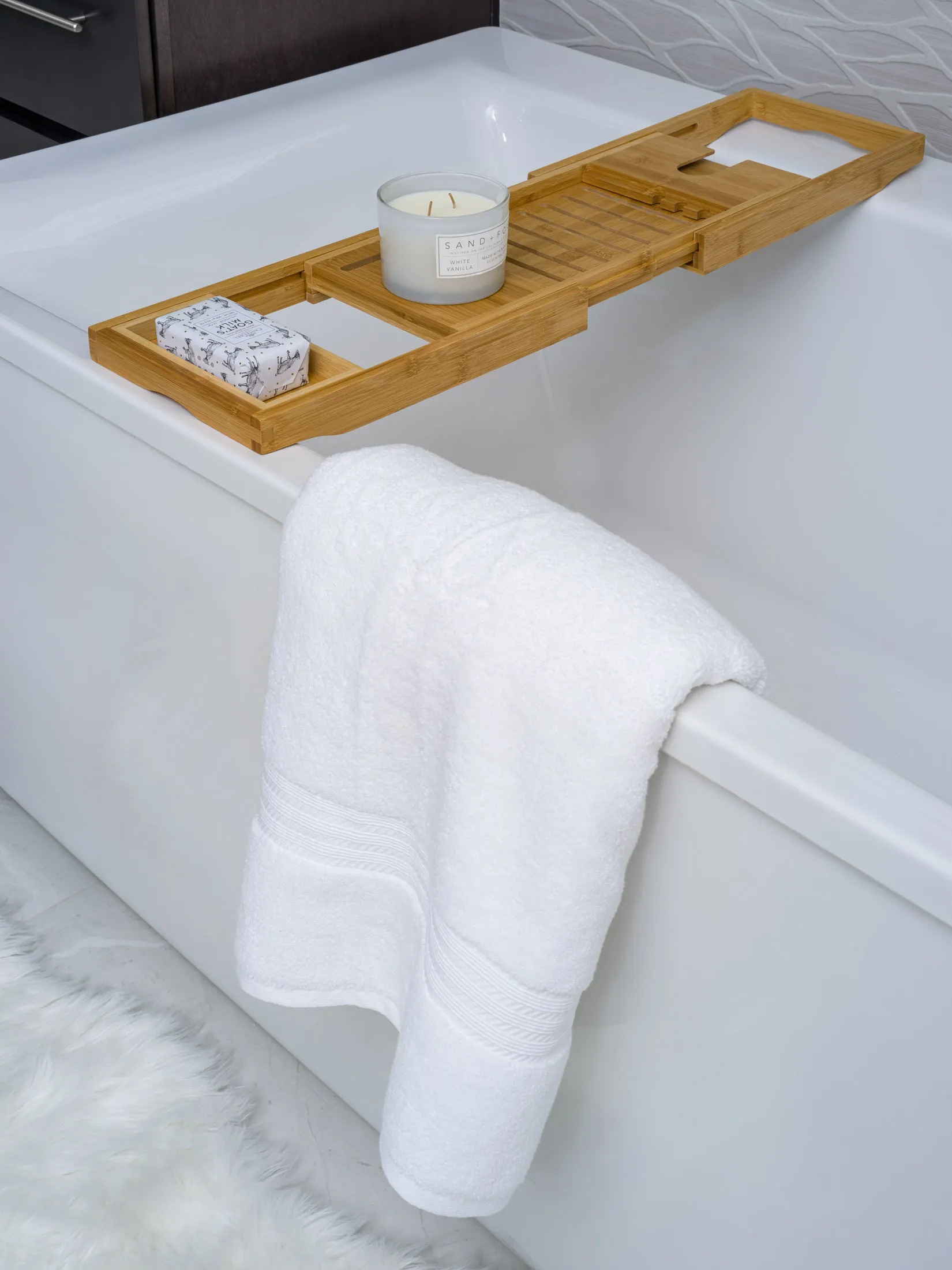 A sleek white bathtub with a bamboo tray holding a scented candle and soap, plus a plush white towel. Staged by Stately in Las Vegas to showcase spa-like luxury and meticulous interior design.