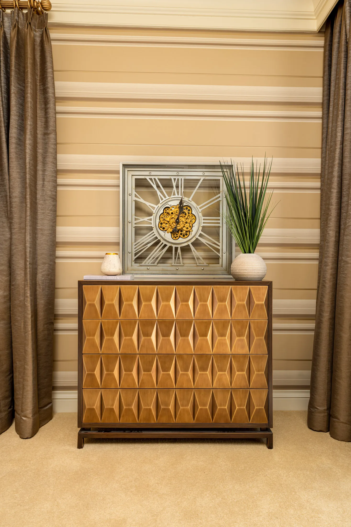 A honey-toned chest with a raised, diamond-like pattern on the drawers. A decorative clock and a small plant in a textured vase sit on top.
