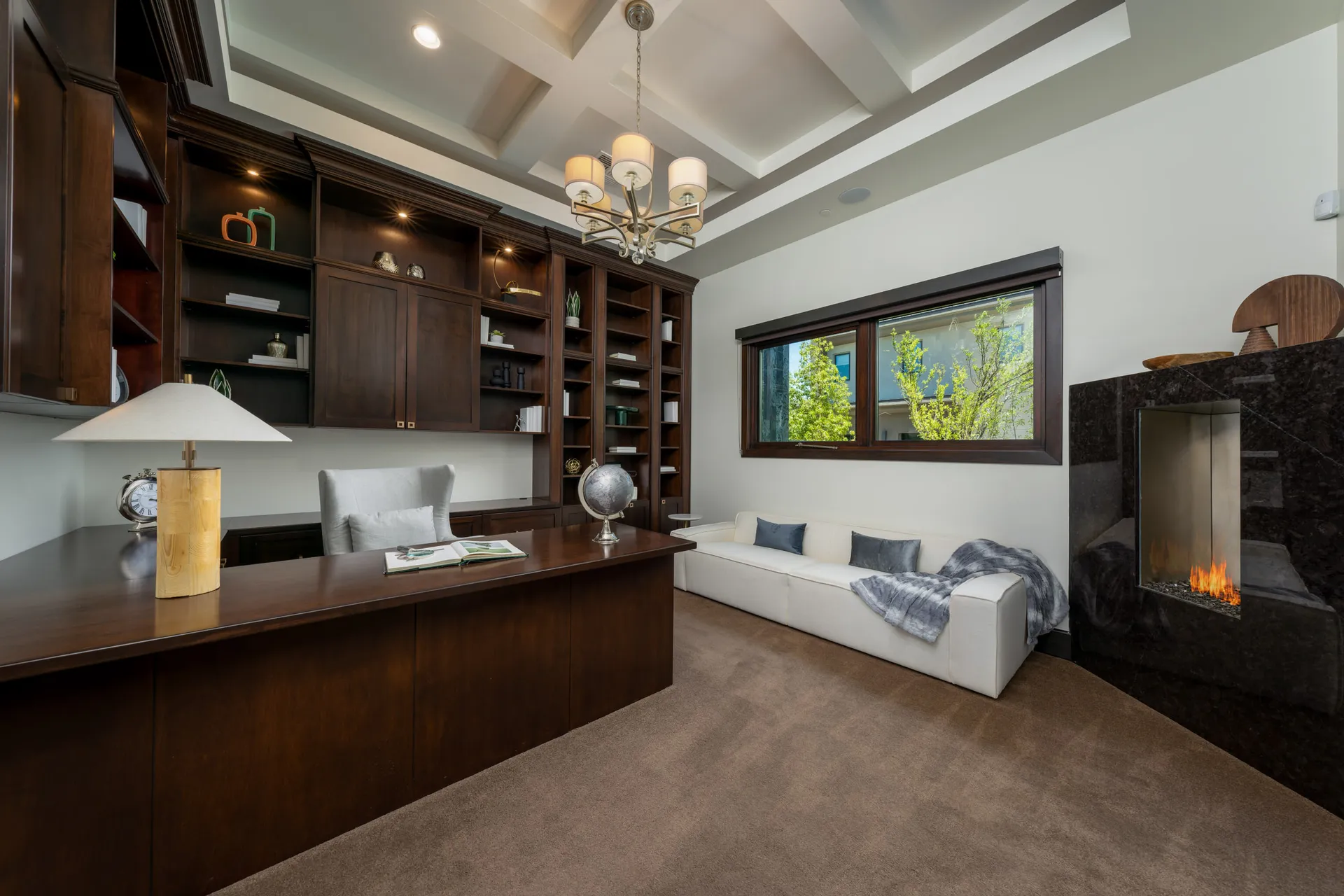 Luxurious home office with large wooden desk, bookshelves, fireplace, and elegant decor.