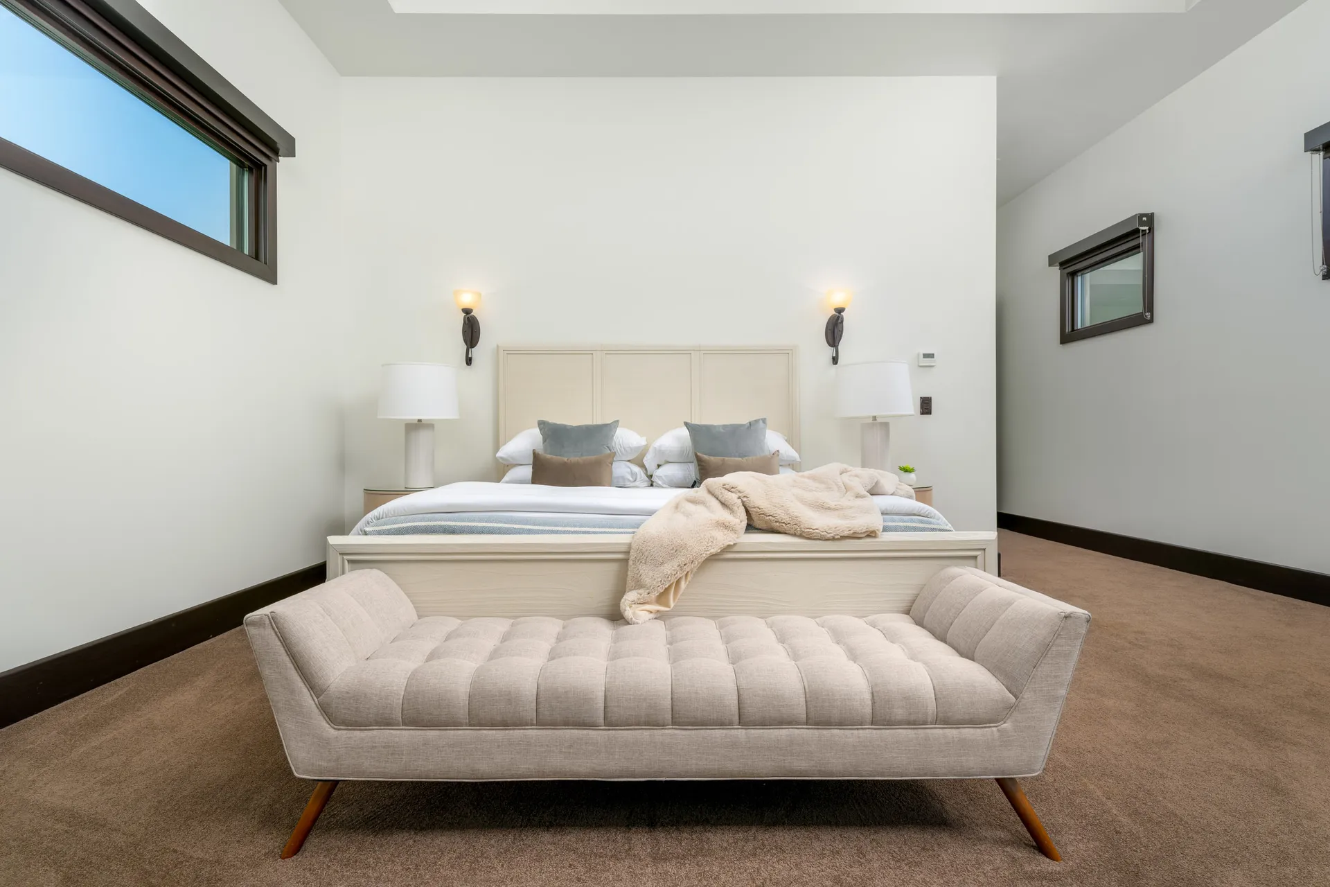 Minimalist bedroom with large bed, bench, and neutral color palette.