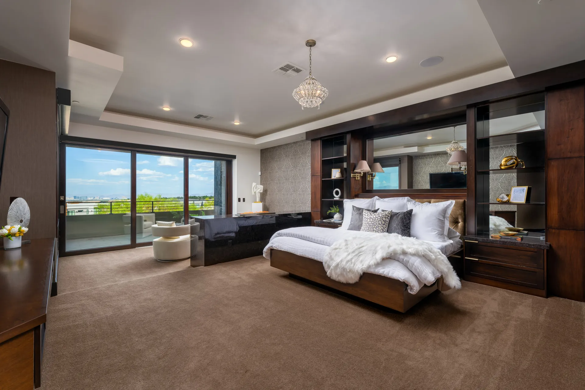 Luxurious bedroom with large bed, plush pillows, chandelier, and outdoor view.