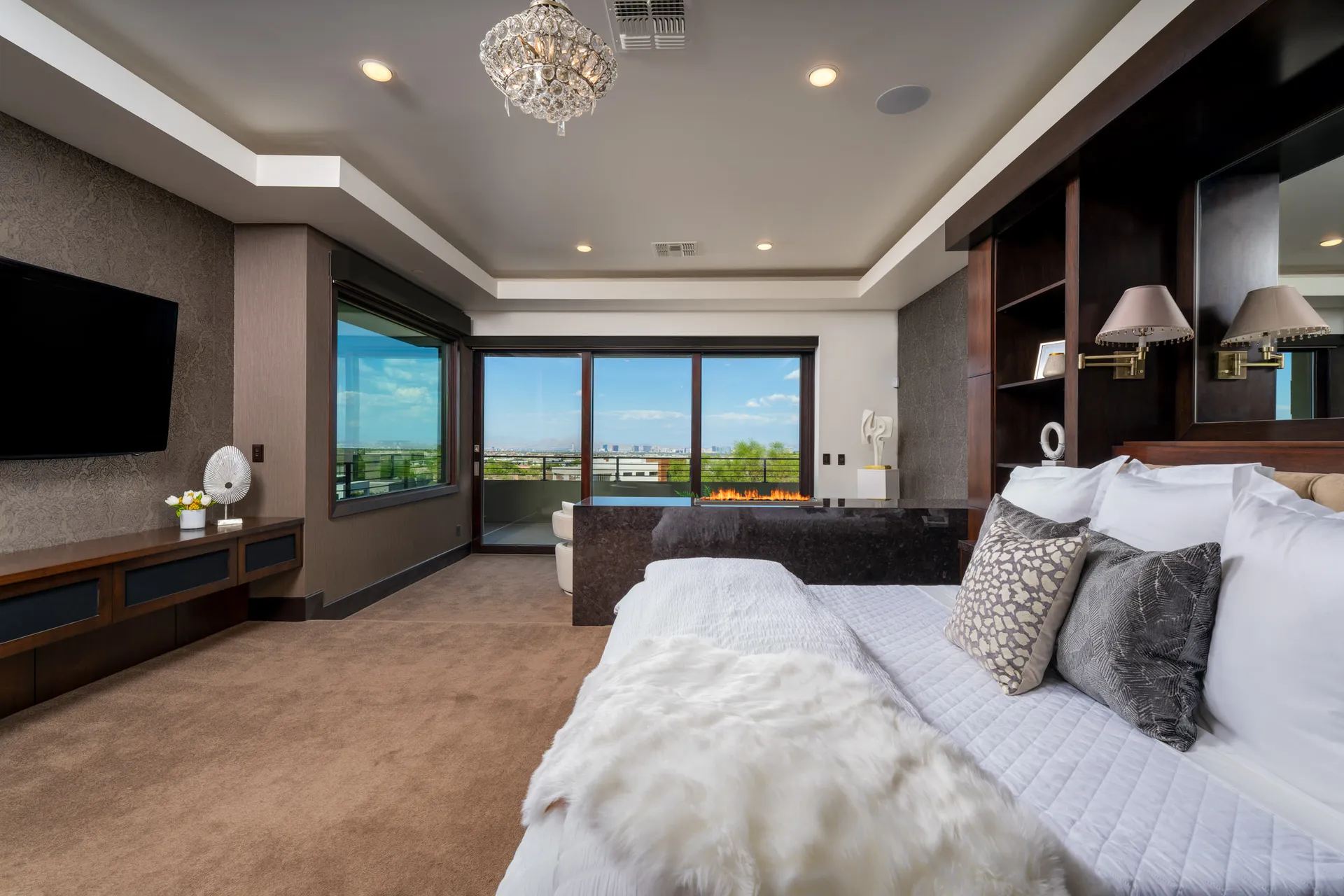 Luxurious bedroom with large bed, plush pillows, chandelier, and outdoor view.
