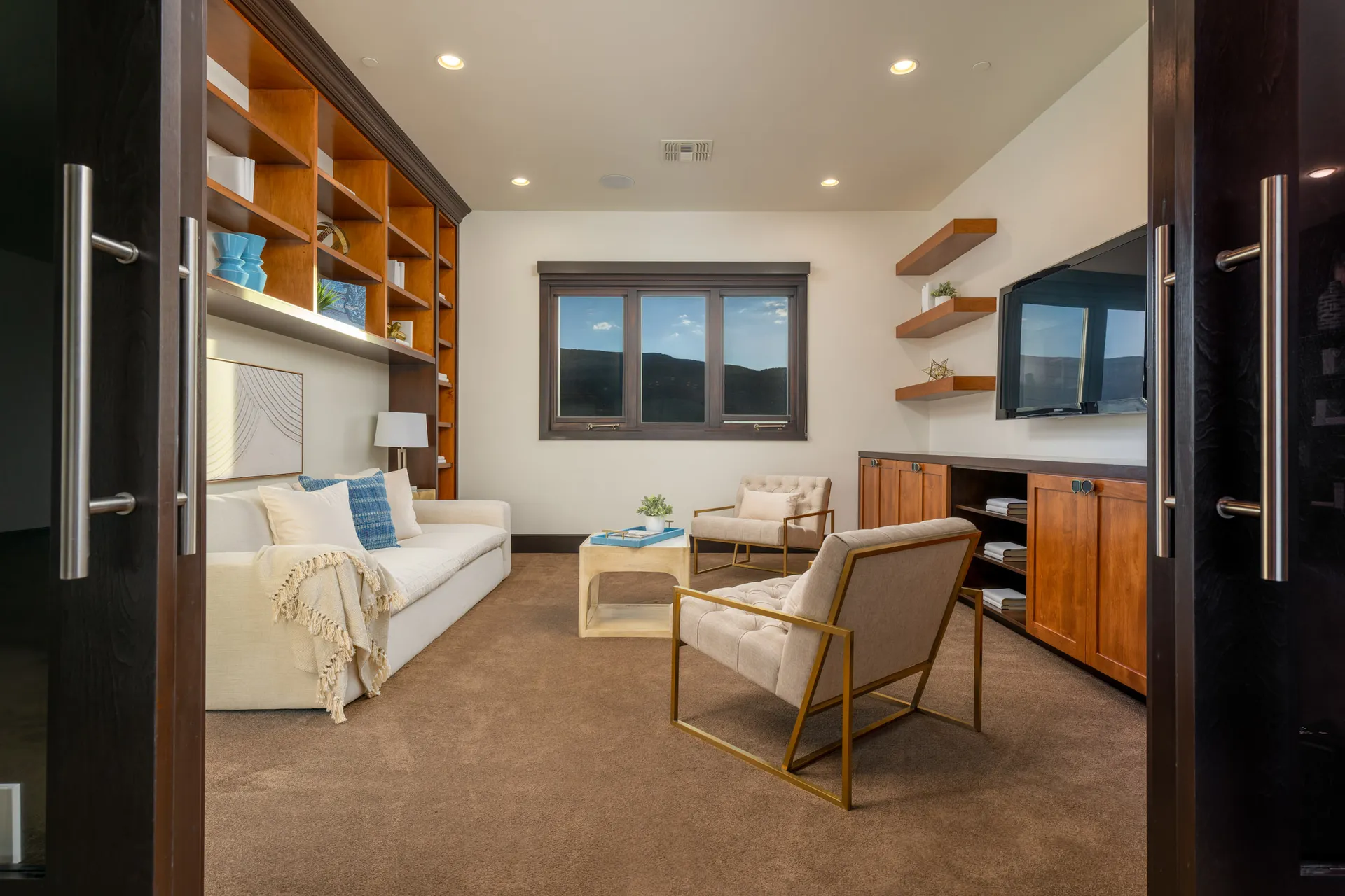 Well-lit room with white sofa, blue throw pillows, wooden coffee table, and built-in wooden bookshelf.