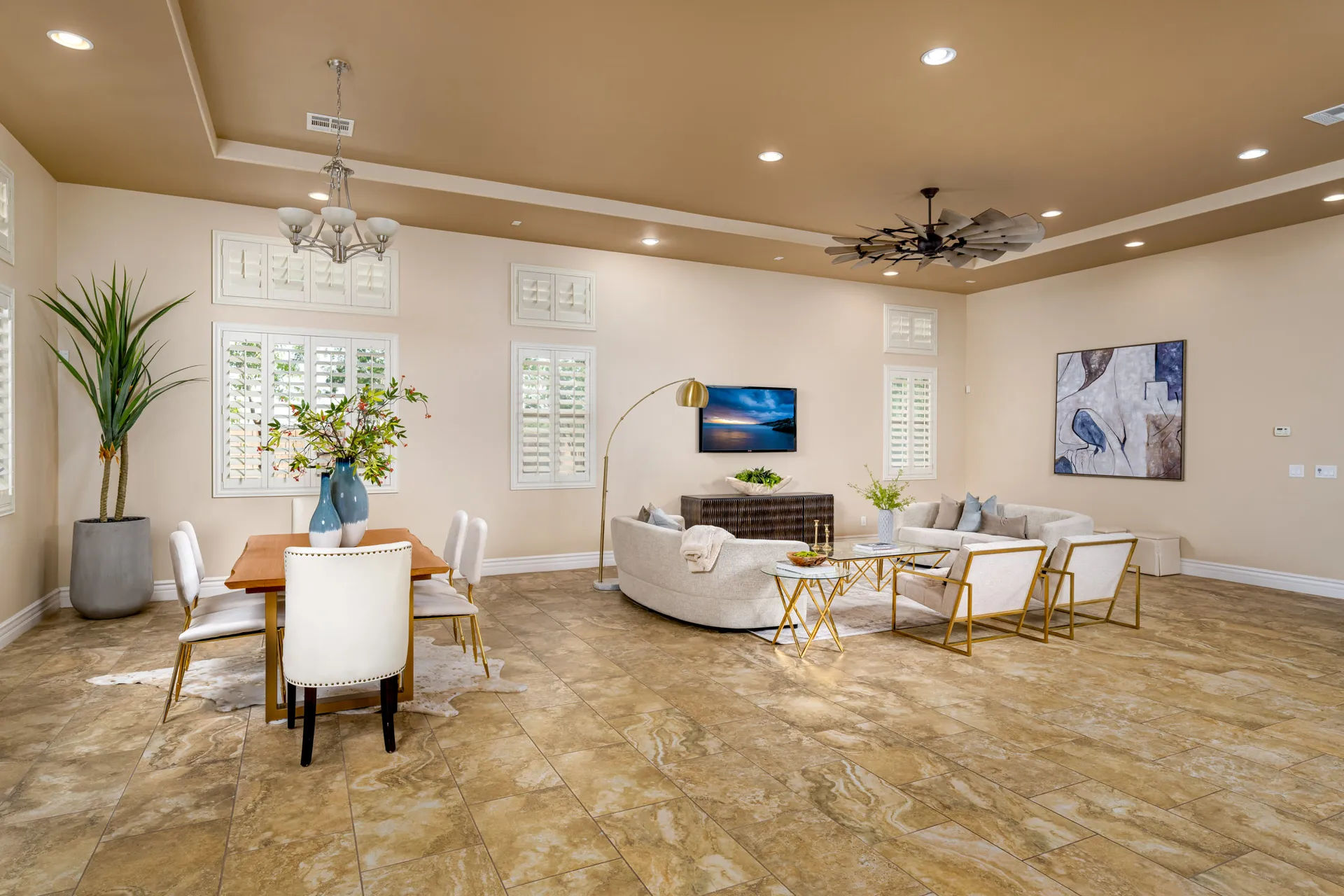 A spacious living and dining area with a curved sofa, gold accent tables, and a wooden dining table under a neutral-toned ceiling.