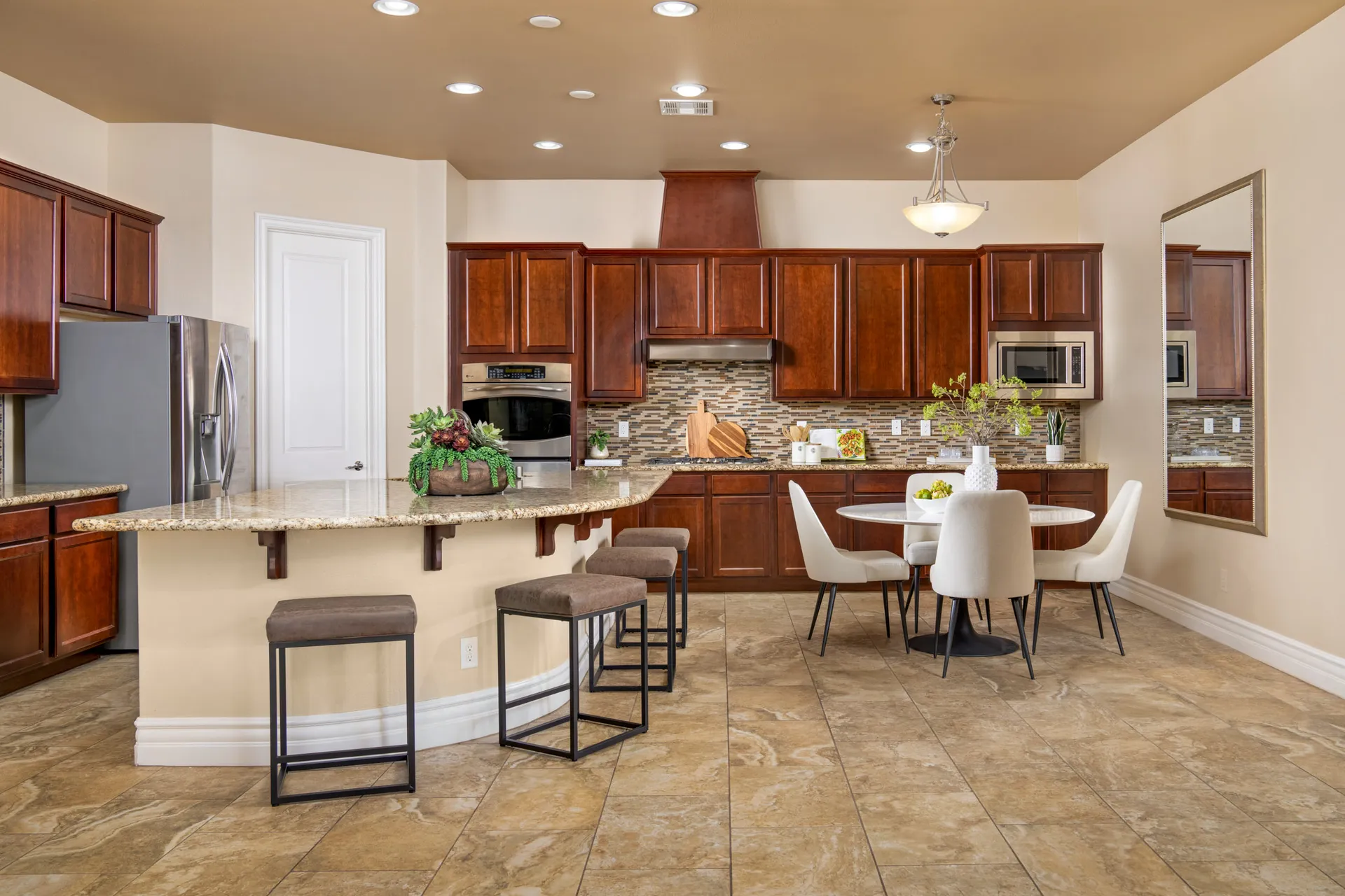 A spacious kitchen with warm wood cabinets, a mosaic backsplash, a granite peninsula with bar stools, and a round dining table with upholstered chairs.