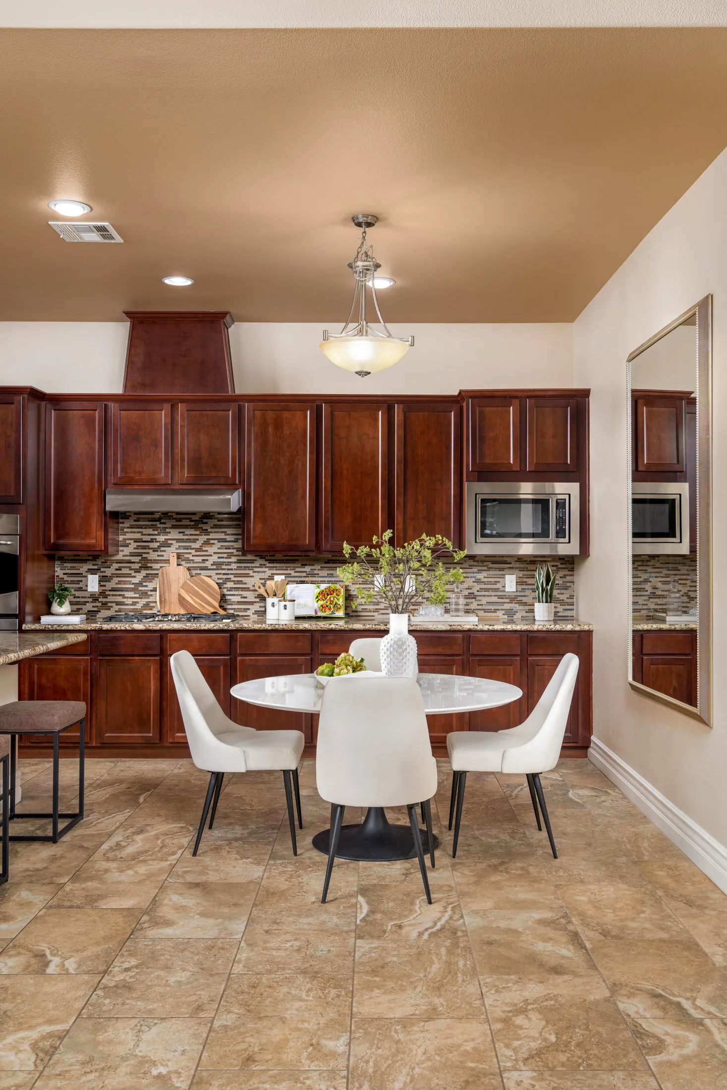 A wood-paneled kitchen with a mosaic backsplash, round white dining table, and upholstered chairs under a hanging light fixture.