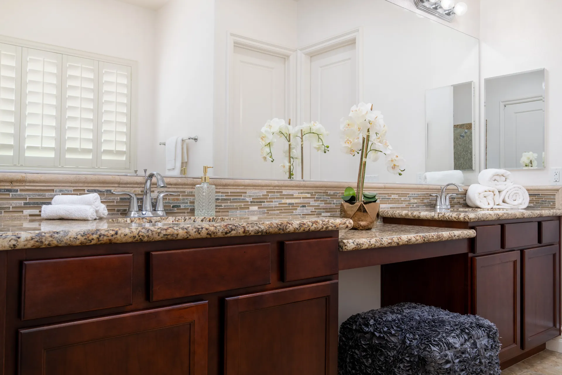 A bathroom vanity with mosaic tile backsplash, granite countertops, and a white orchid on the counter.