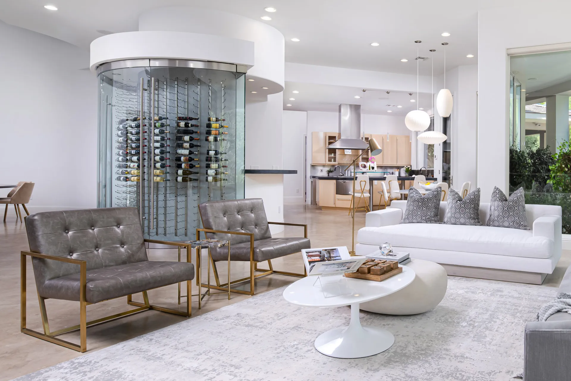 A modern living room featuring plush seating, gold-accented chairs, a sleek white coffee table, and a glass-enclosed wine display.