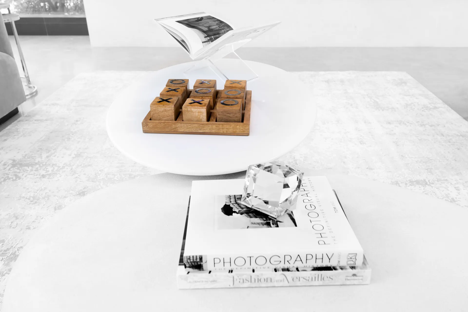 A black-and-white styled coffee table featuring stacked books, a crystal accent, and a wooden tic-tac-toe game.
