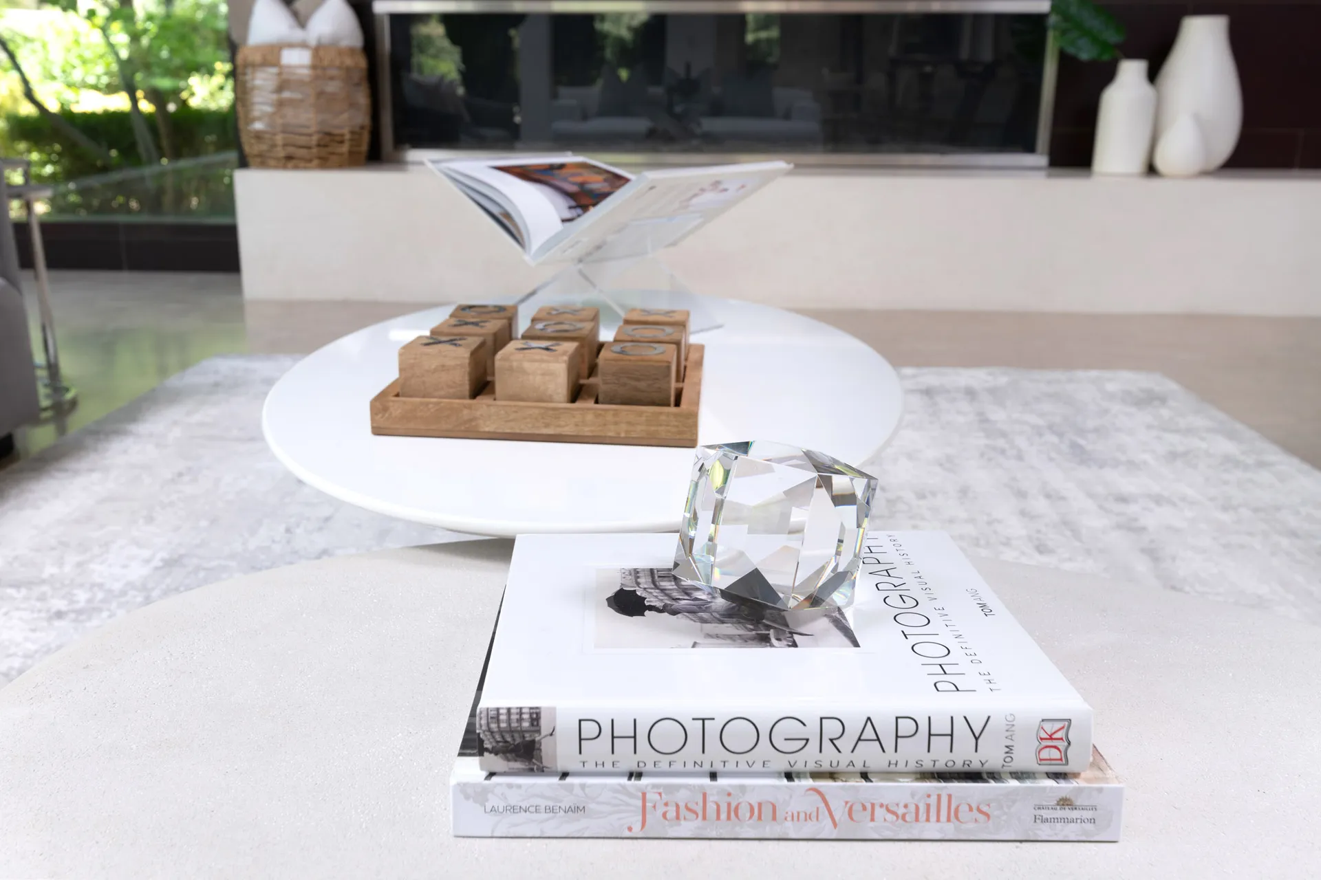 A modern coffee table styled with stacked books, a crystal accent, and a wooden tic-tac-toe game.