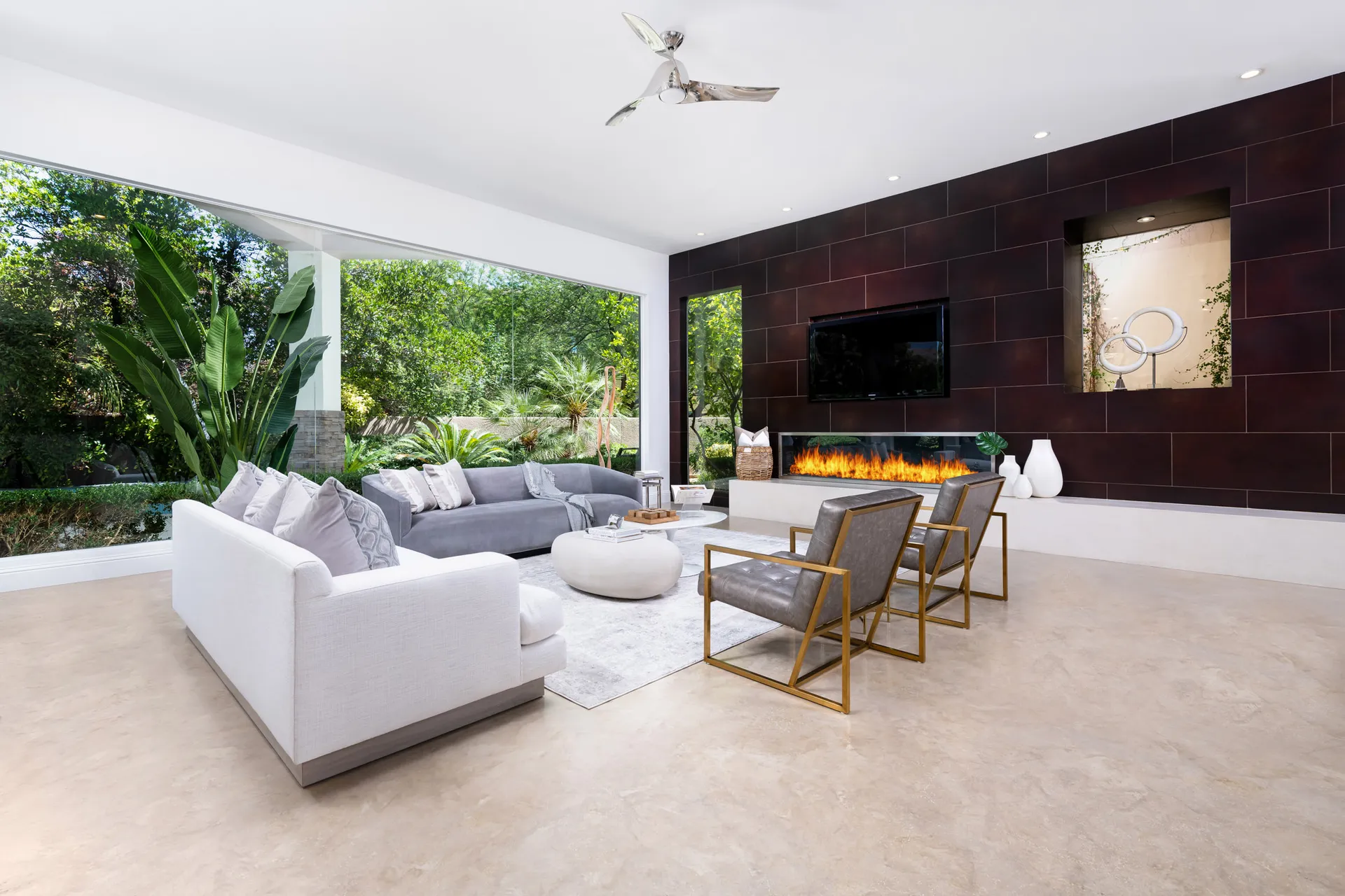 A modern living room with a sleek fireplace, plush seating, and floor-to-ceiling windows offering lush garden views.