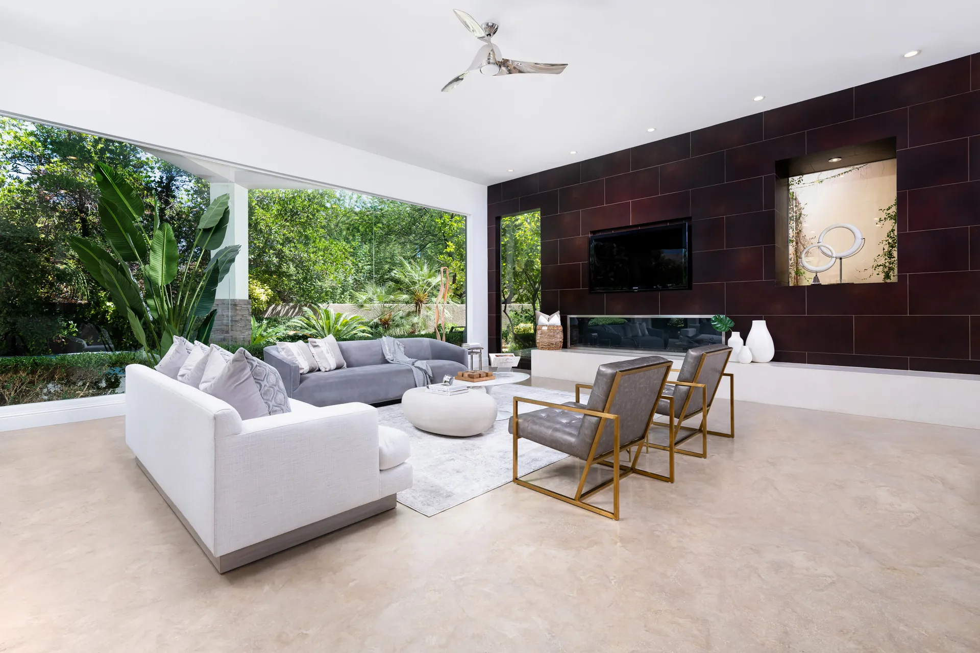 A sophisticated living room with a dark accent wall, plush seating, and floor-to-ceiling windows showcasing lush greenery.