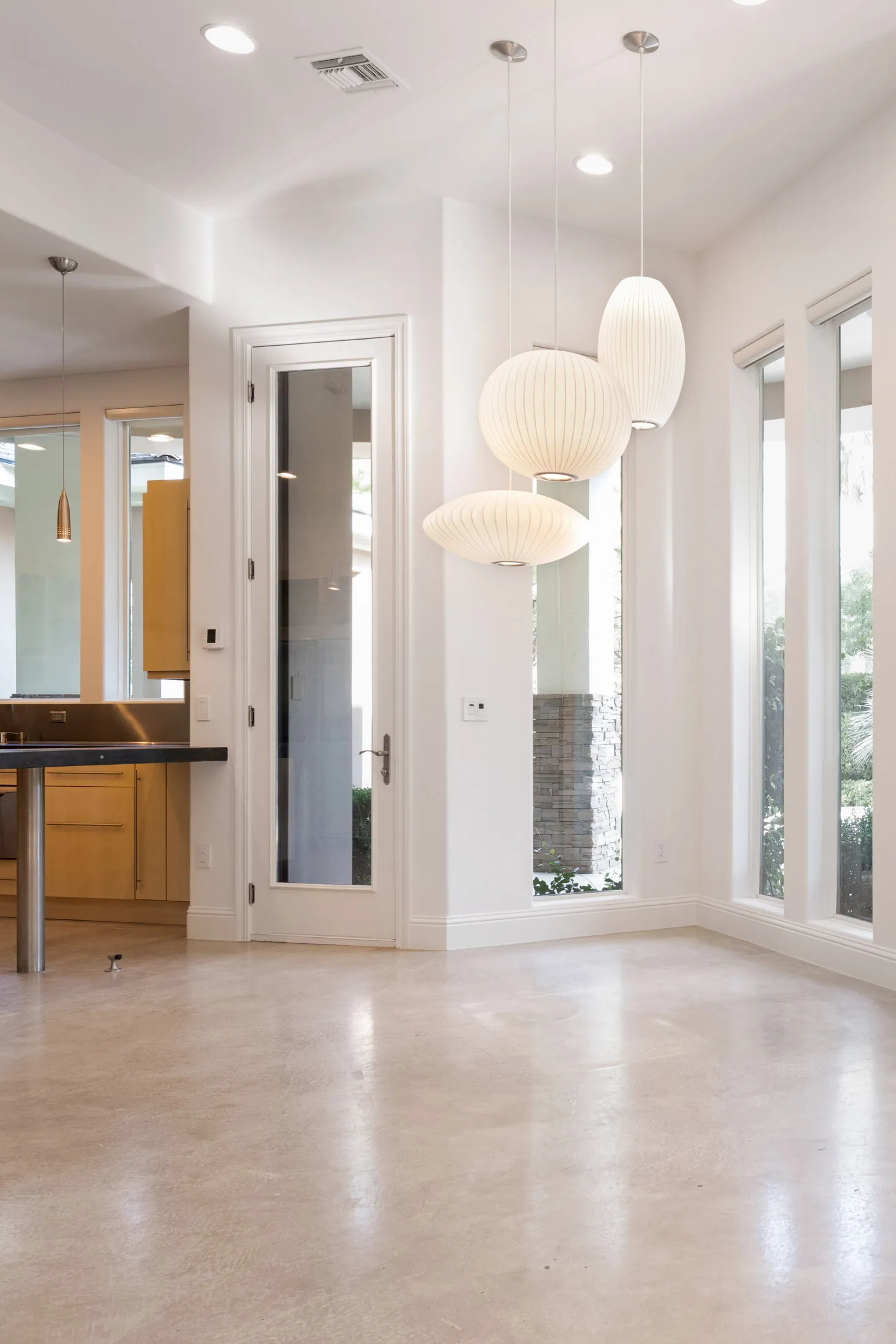 An empty dining area with large windows, white walls, and modern pendant lighting, awaiting furnishing.