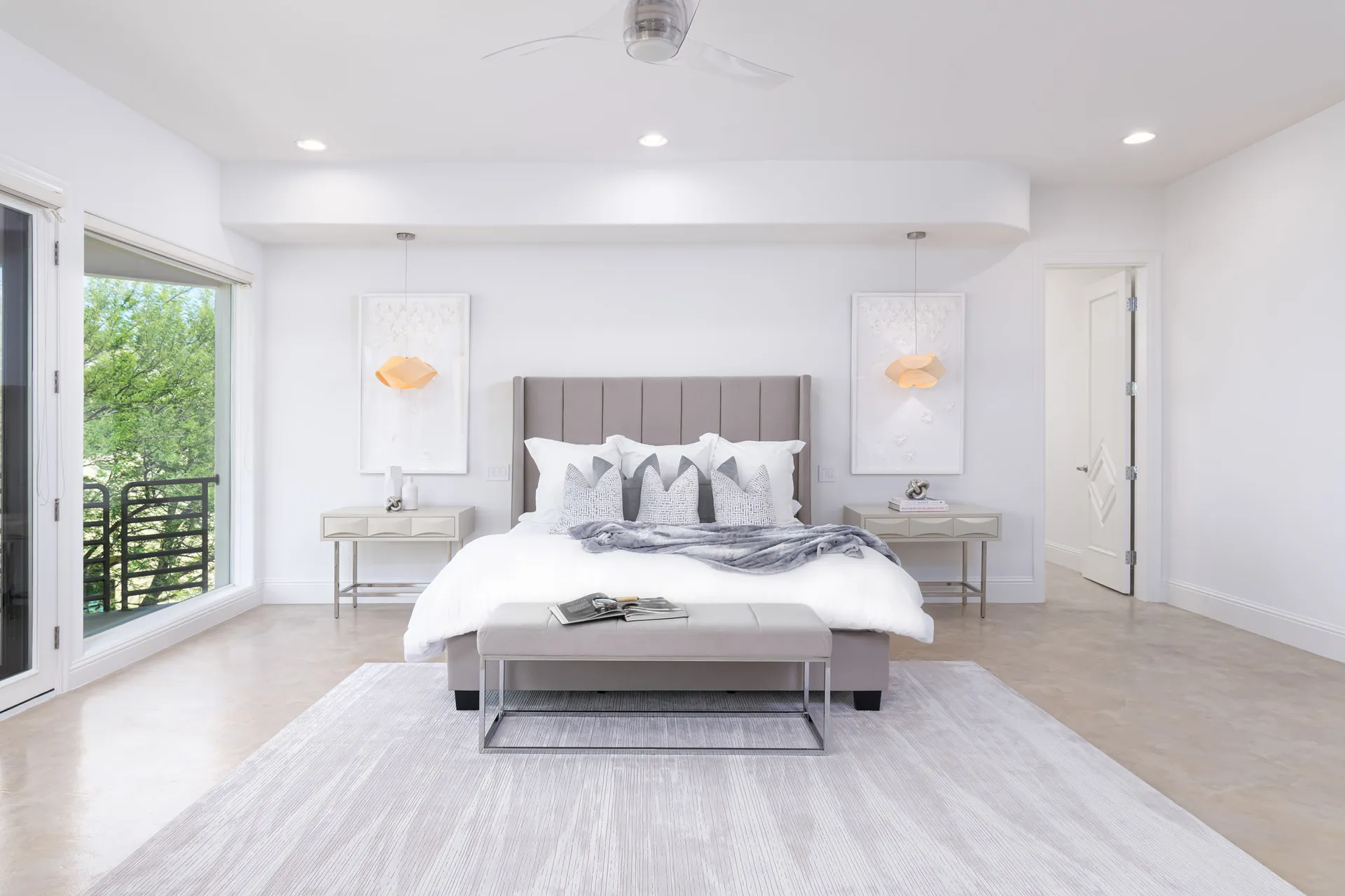 A beautifully staged master bedroom featuring a tufted gray bed, crisp white bedding, modern nightstands, and soft lighting.
