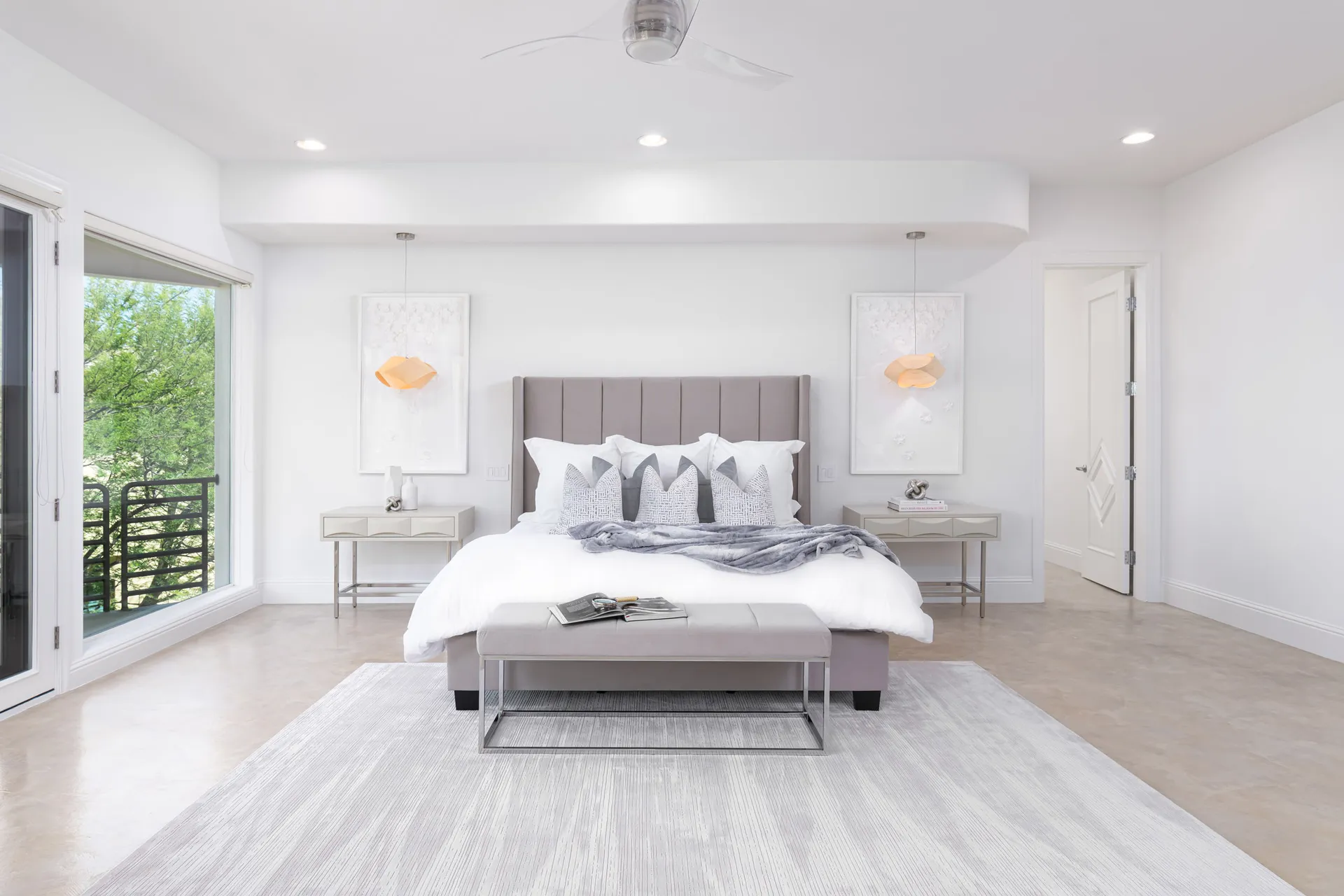 A bright master bedroom featuring a tufted gray bed, crisp white bedding, a plush bench, and modern nightstands with stylish decor.
