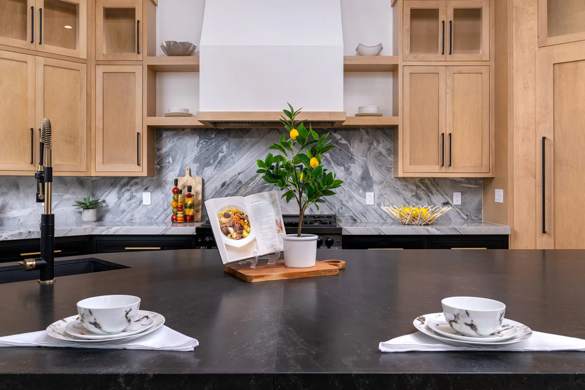 Kitchen with wooden cabinets, a marble backsplash, and a black countertop featuring an open cookbook and a potted plant, creating a warm and inviting kitchen space.