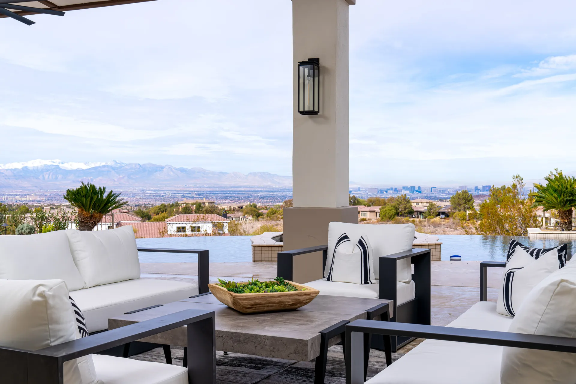 Outdoor seating area with a sofa, chairs, and a coffee table. The area overlooks a scenic view of mountains and a pool, offering a relaxing and inviting outdoor space.