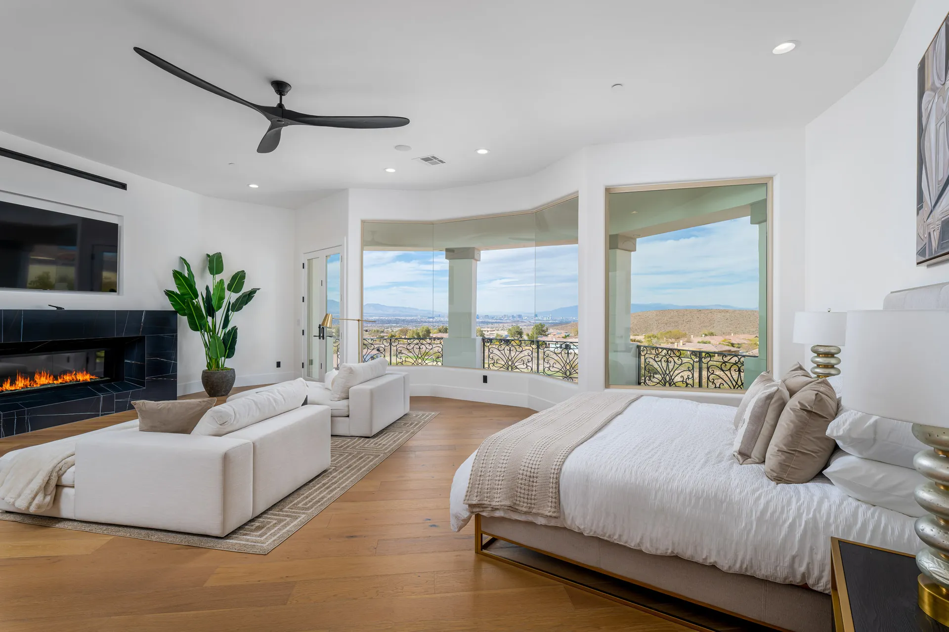 A spacious bedroom with white seating, a sleek fireplace, and large windows revealing a wide desert view.