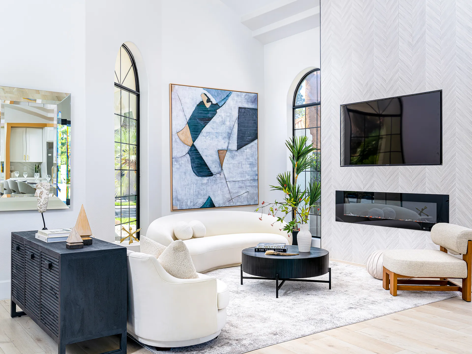 A bright living area with an arched window, a curved white sofa, and a herringbone-pattern fireplace showcasing a modern electric fireplace.