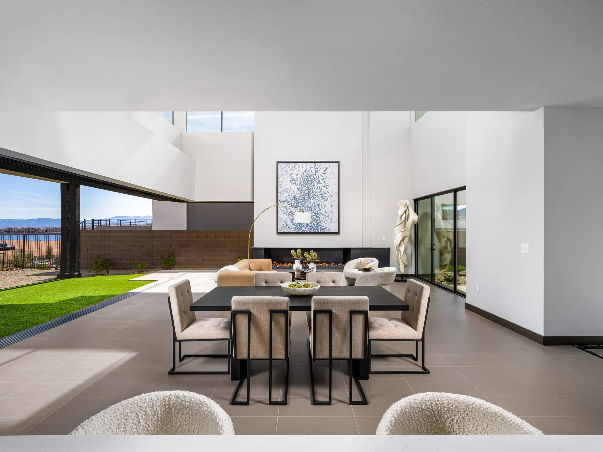 A sleek dining table in a large open space, seamlessly transitioning to an outdoor area with desert views and neutral modern seating.
