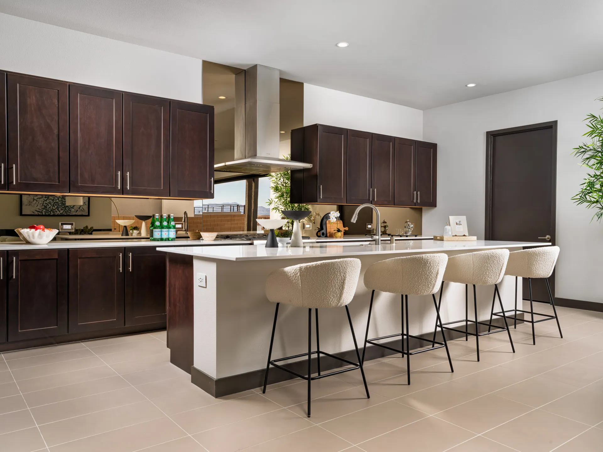 A modern kitchen with dark wood cabinets, a stainless range hood, and an island topped by four plush barstools.