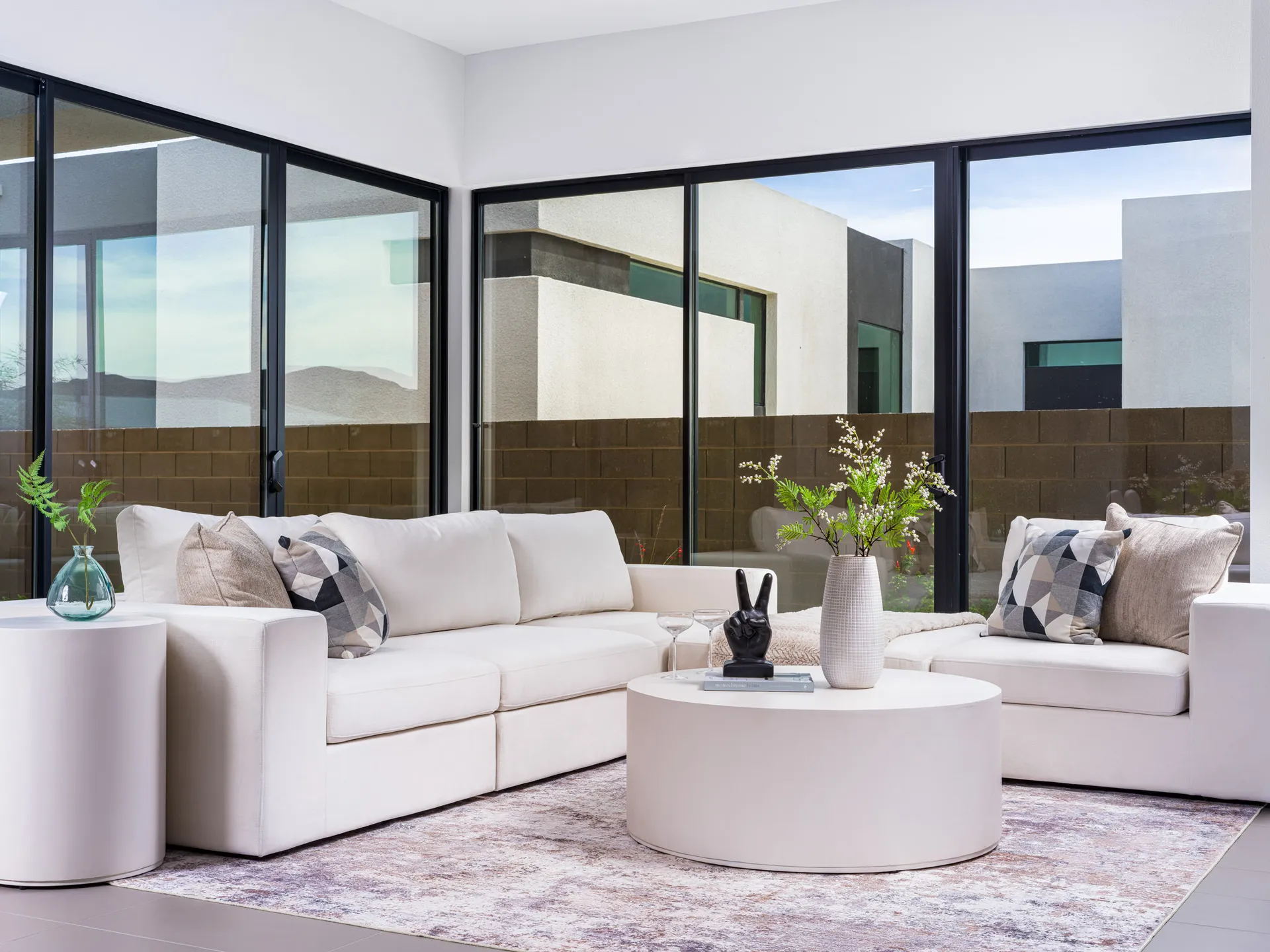 A white sectional sofa with geometric pillows by floor-to-ceiling windows, centered around a round coffee table.