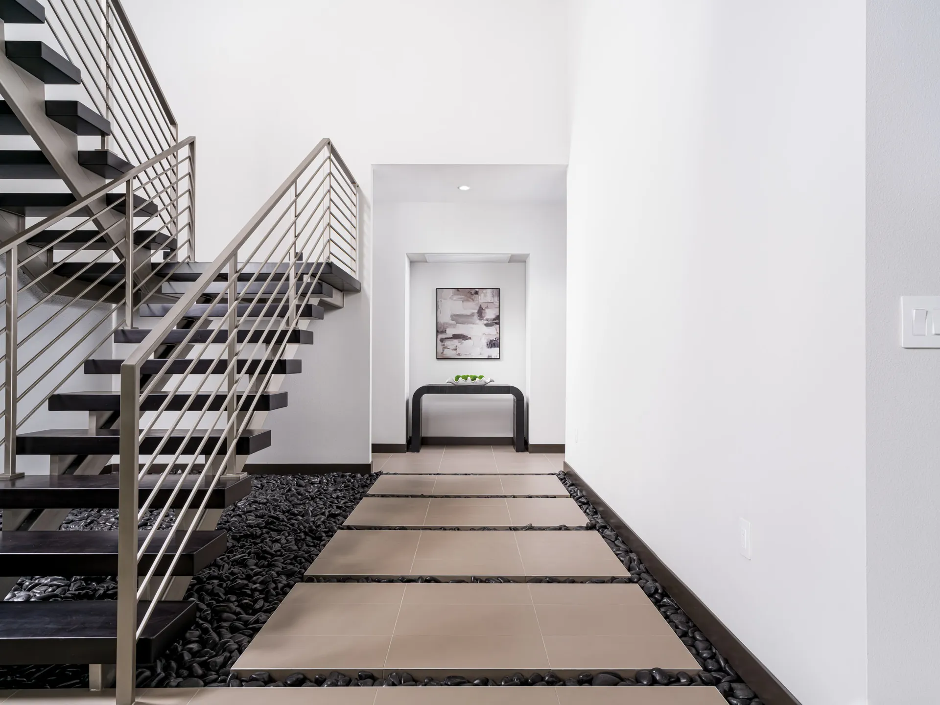 A floating staircase with dark wood steps and a pebble-lined walkway leading to a sleek console table.