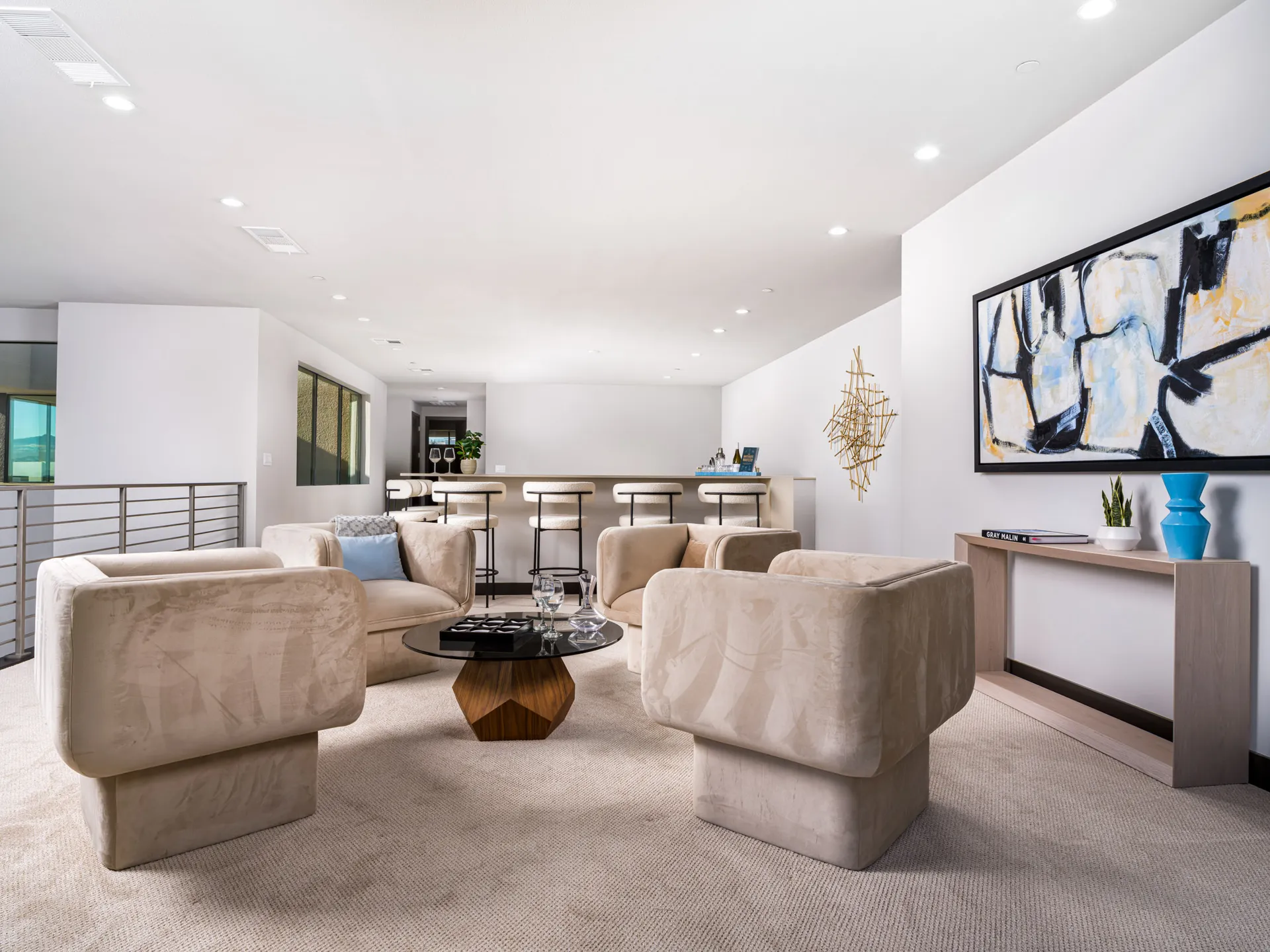 A bright open loft area with plush, sand-colored lounge chairs, a round coffee table, and a bar counter in the background.