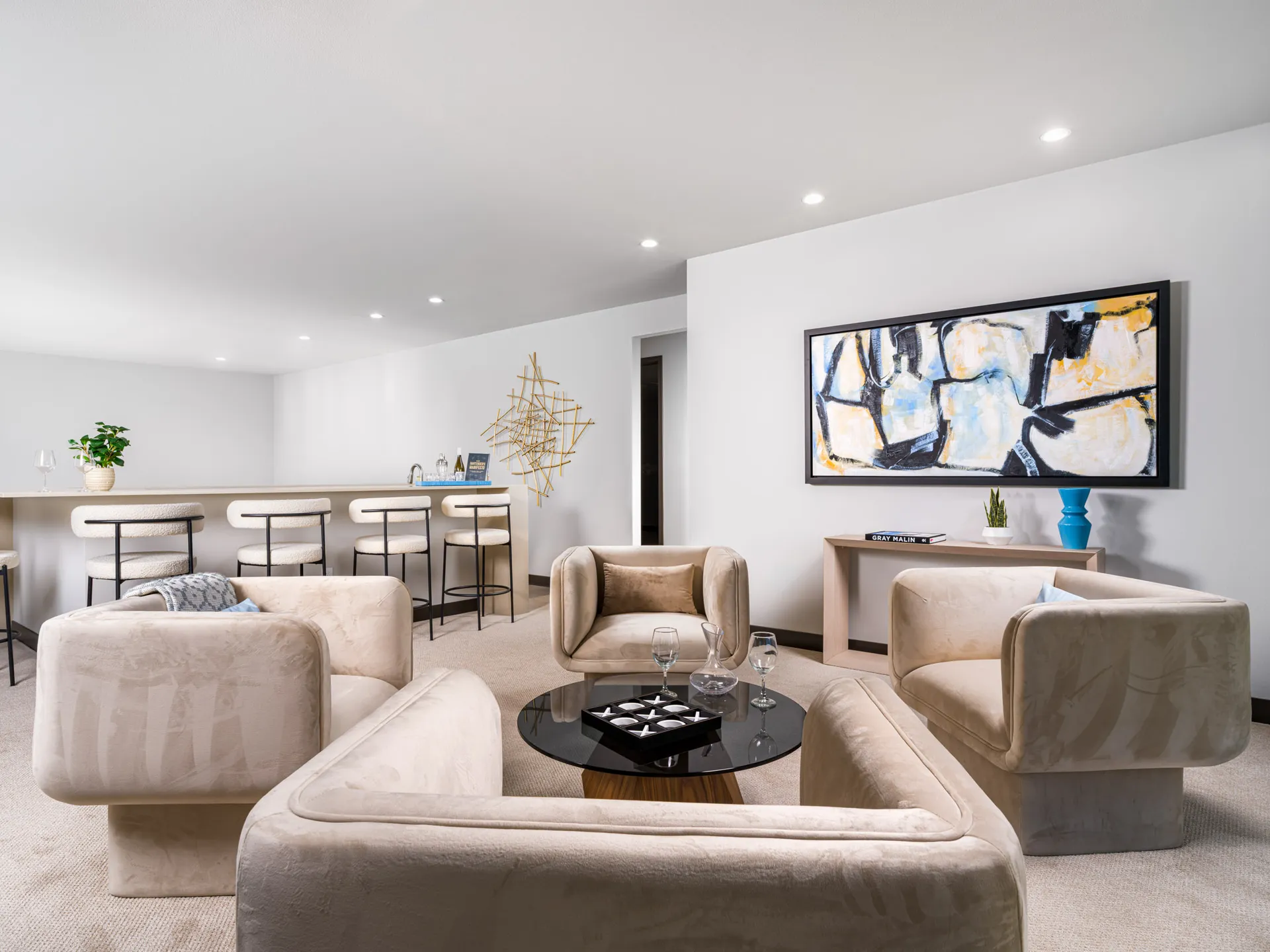 A bright open loft area with plush, sand-colored lounge chairs, a round coffee table, and a built-in bar counter.