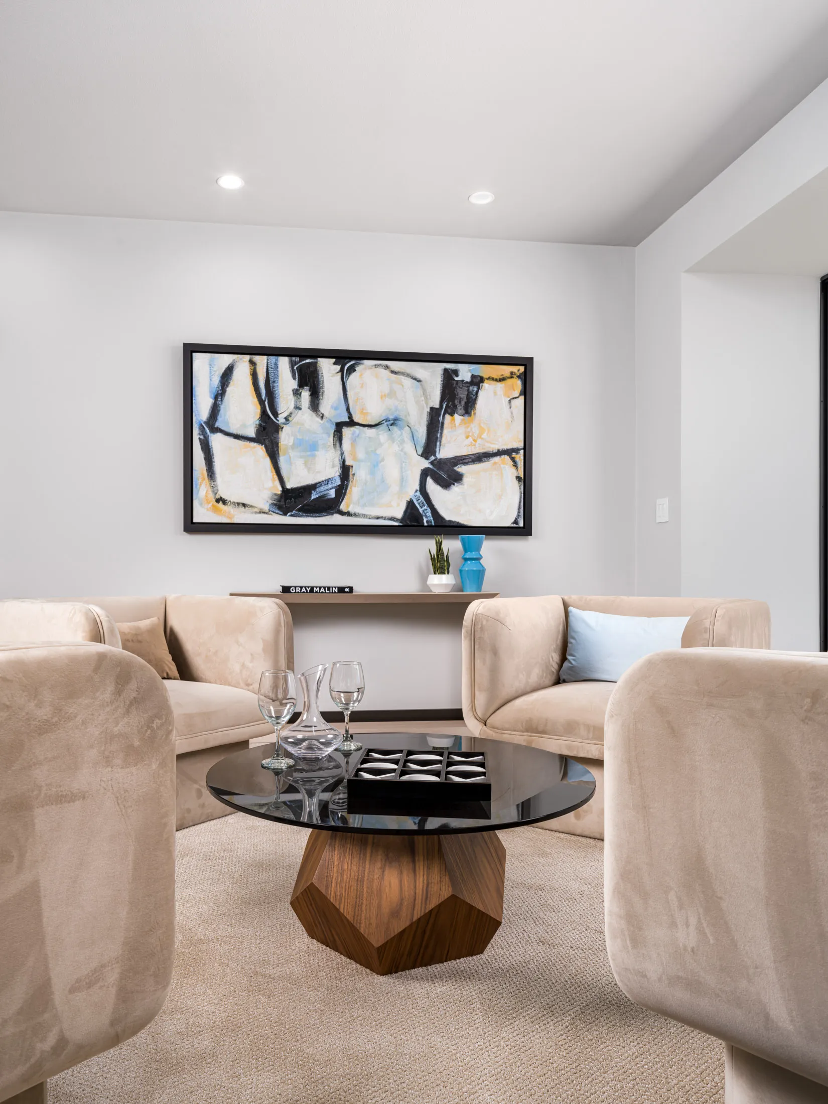 A set of plush sand‑colored chairs around a faceted wood coffee table, accented by abstract wall art.