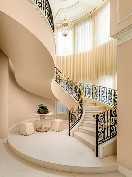 A stunning curved staircase with ornate wrought iron railings, elegant drapery, and a luxurious chandelier in a grand foyer.