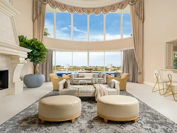 A grand living room with soaring windows, elegant drapery, plush seating, and a neutral color palette overlooking a stunning outdoor view.