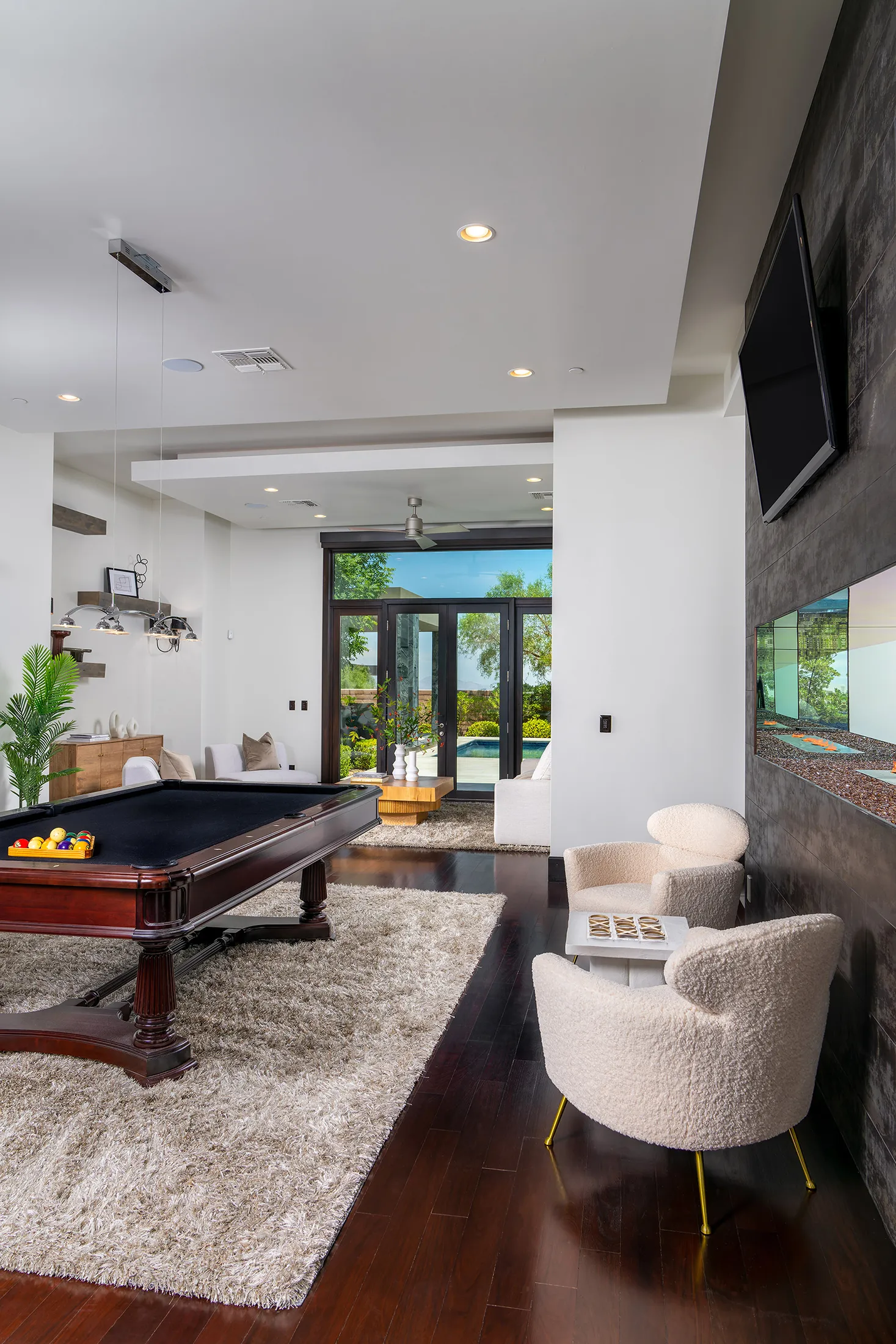 A spacious game room with a classic pool table on a plush rug, modern seating, and large doors leading to an outdoor area.