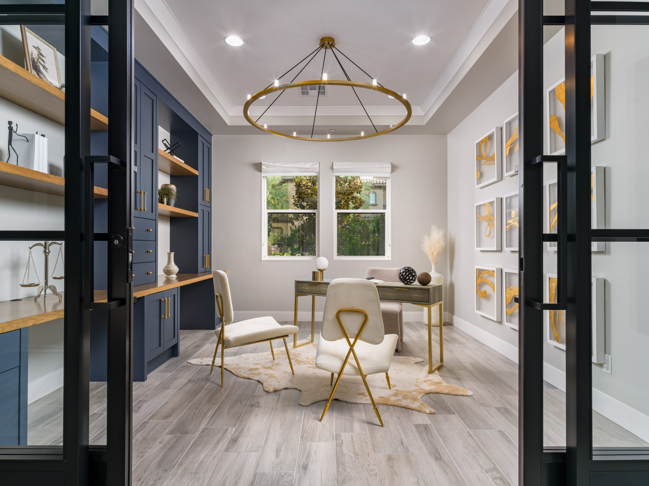 Home Staging Las Vegas: A stylish home office featuring blue built-in shelving, a gold chandelier, modern artwork, and elegant furniture in a staged interior.