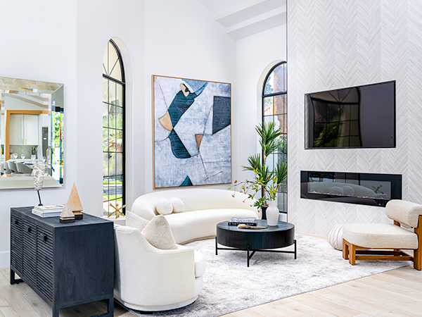 A beautifully staged living room featured on Stately’s homepage, showcasing a modern curved sofa, abstract artwork, arched windows, a sleek black console table, and a contemporary fireplace with a mounted TV, embodying the elegance and sophistication of Stately’s luxury home staging services.