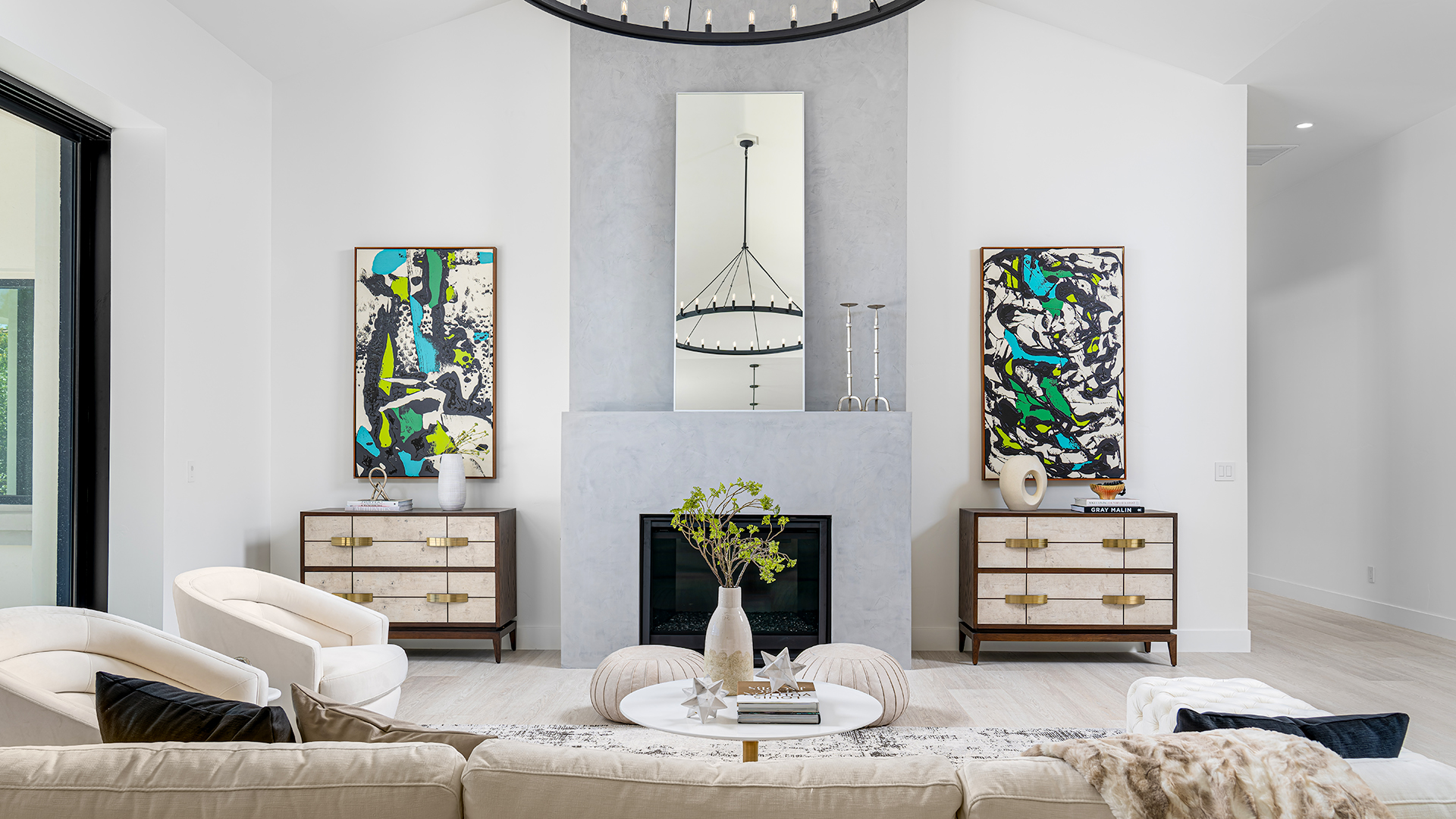 Living room with a white sofa, a round coffee table, a fireplace, and two matching side tables with abstract art above them. The room has a modern and elegant design, creating a comfortable and stylish space for relaxation.