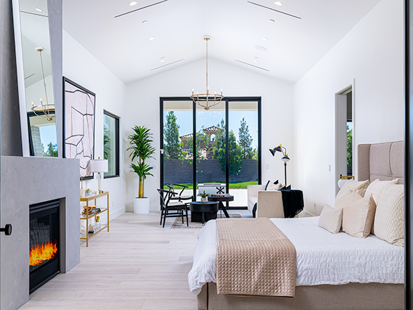 A luxurious master bedroom featured on Stately’s homepage, showcasing a cozy bed with neutral tones, a modern fireplace, large sliding glass doors opening to a scenic backyard, and refined decor that highlights Stately’s expertise in creating serene and sophisticated spaces.