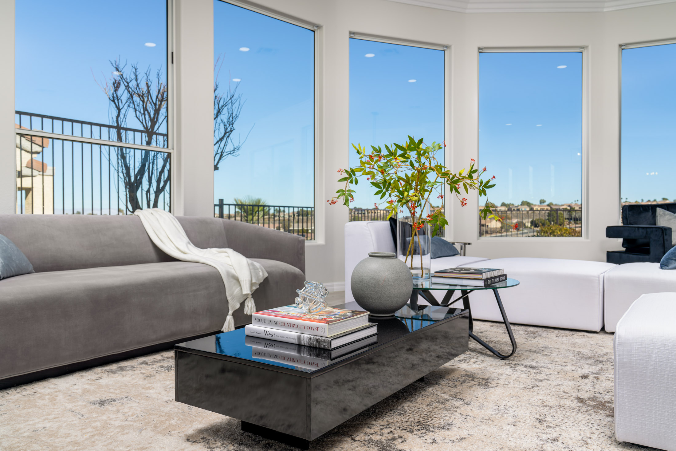 A contemporary living room with a plush gray sofa, black coffee table, modern decor, and large windows showcasing scenic outdoor views.