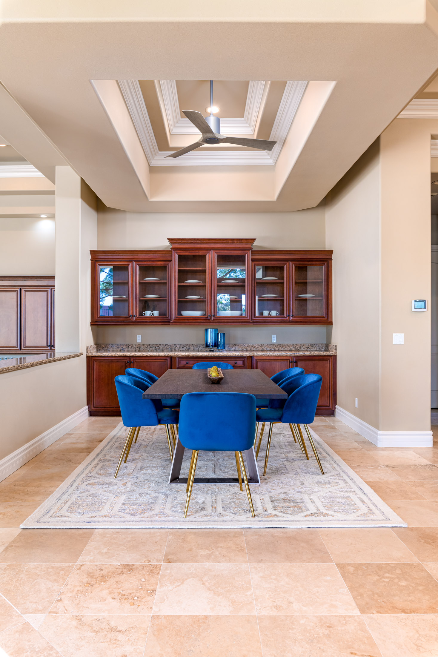 A dining nook featuring a dark wood table, blue velvet chairs with gold legs, and cherry cabinetry in the background.