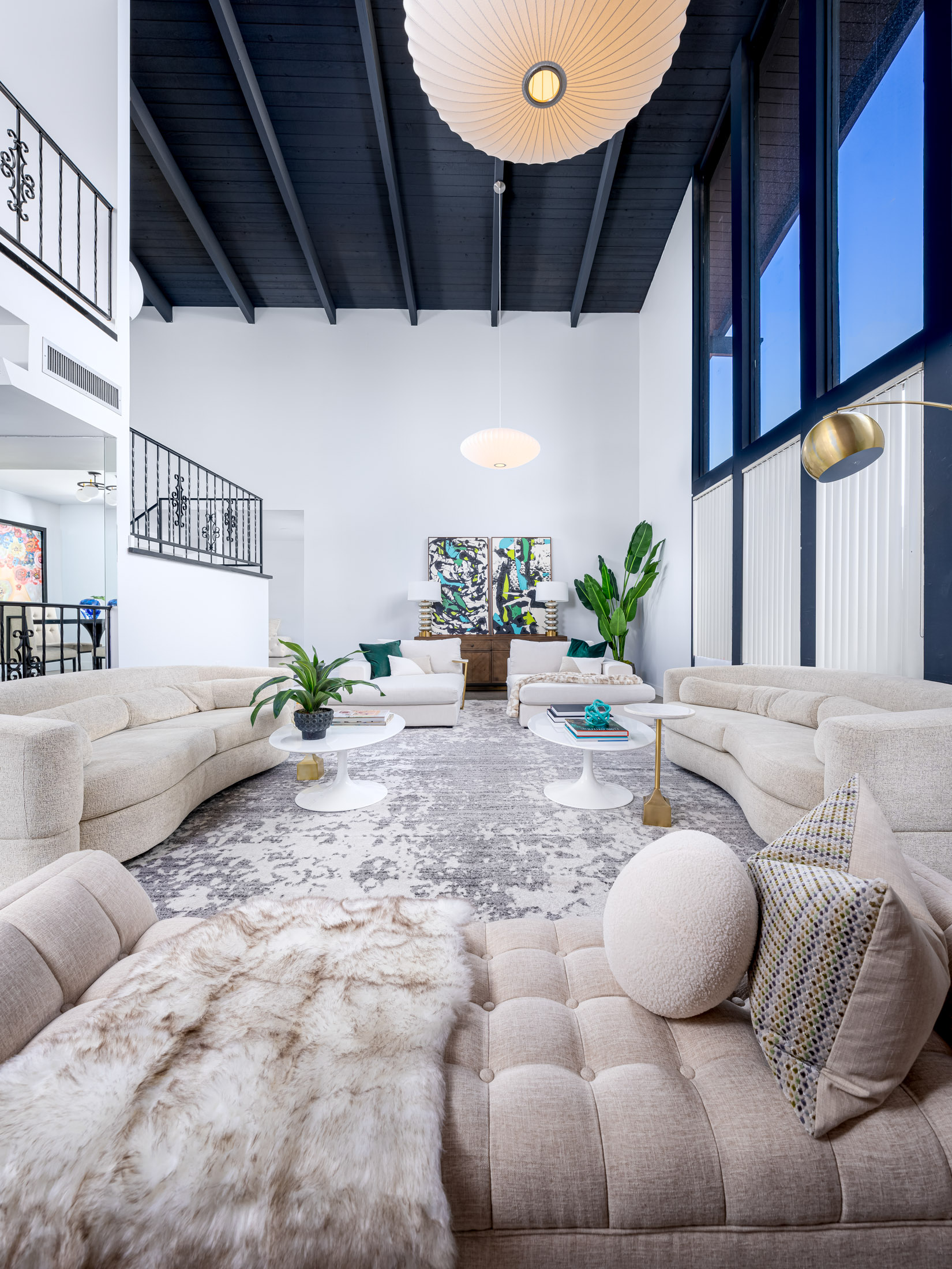 A lofty living area featuring a black vaulted ceiling, curved neutral sofas, and large abstract artwork.