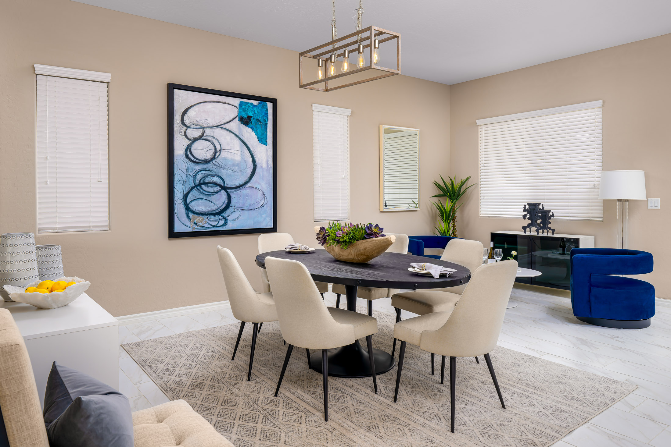 An oval black dining table with white chairs, a wooden bowl of succulents, and large abstract artwork on beige walls.