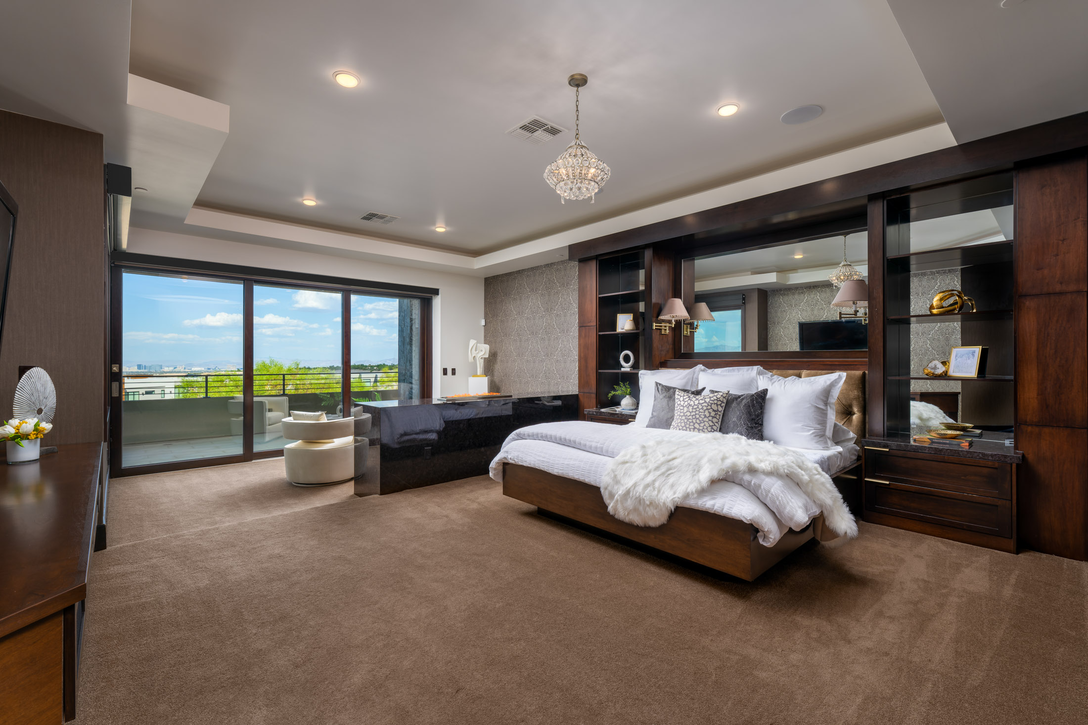Luxurious bedroom with large bed, plush pillows, chandelier, and outdoor view.
